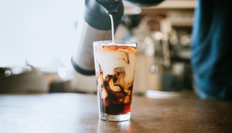 A man pours creamer into his coffee.