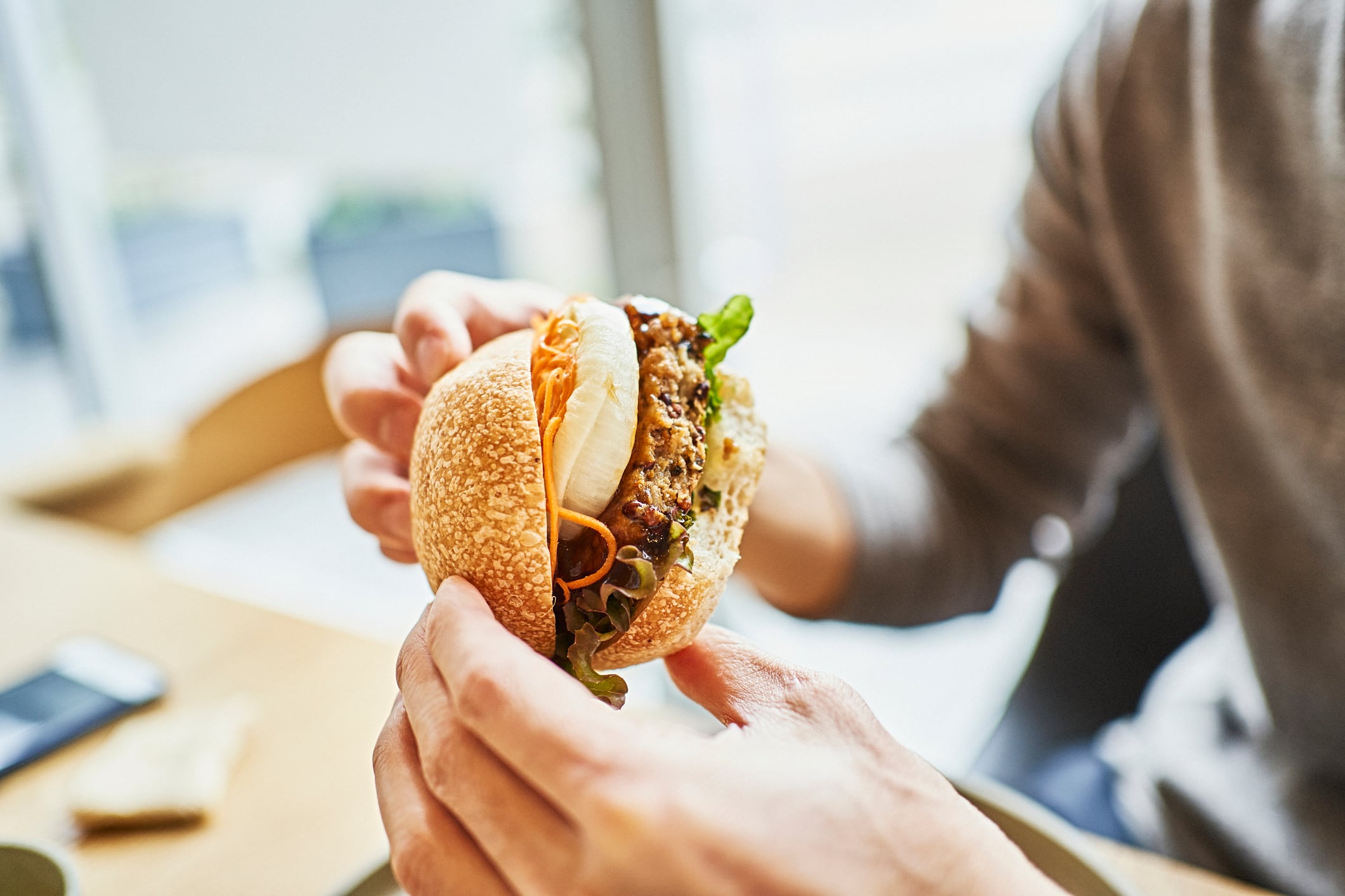 Person eating veggie burger, light background with phone