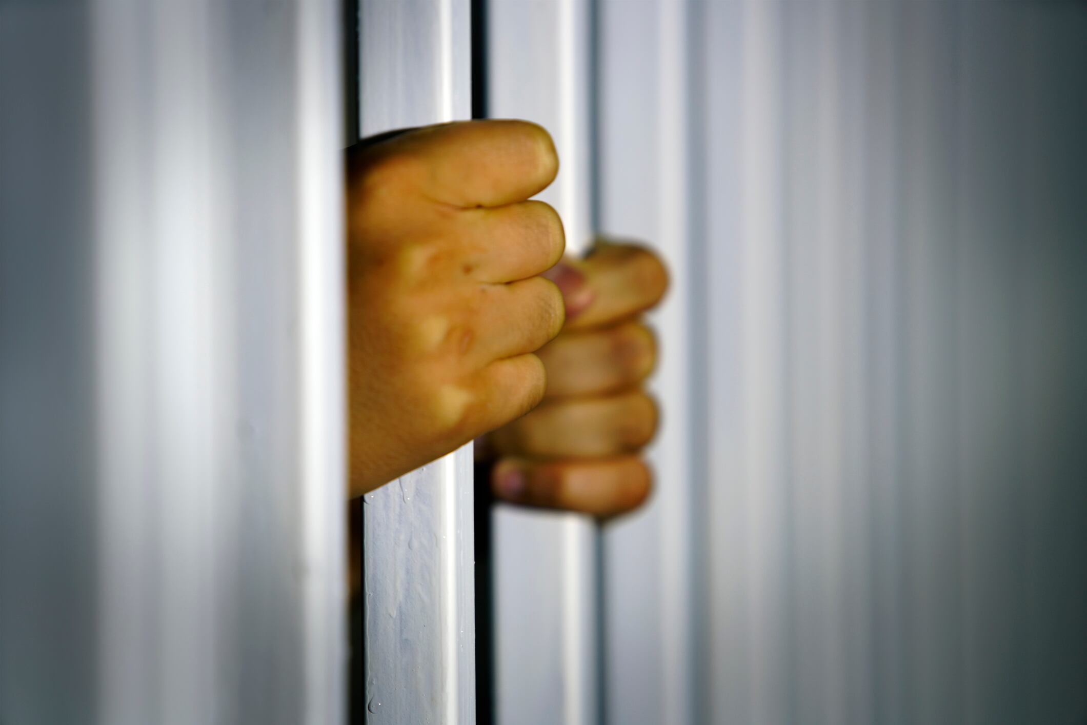 This image captures hands gripping metal bars, conveying feelings of confinement and isolation. The play of light and shadow adds emotional depth to the powerful scene.