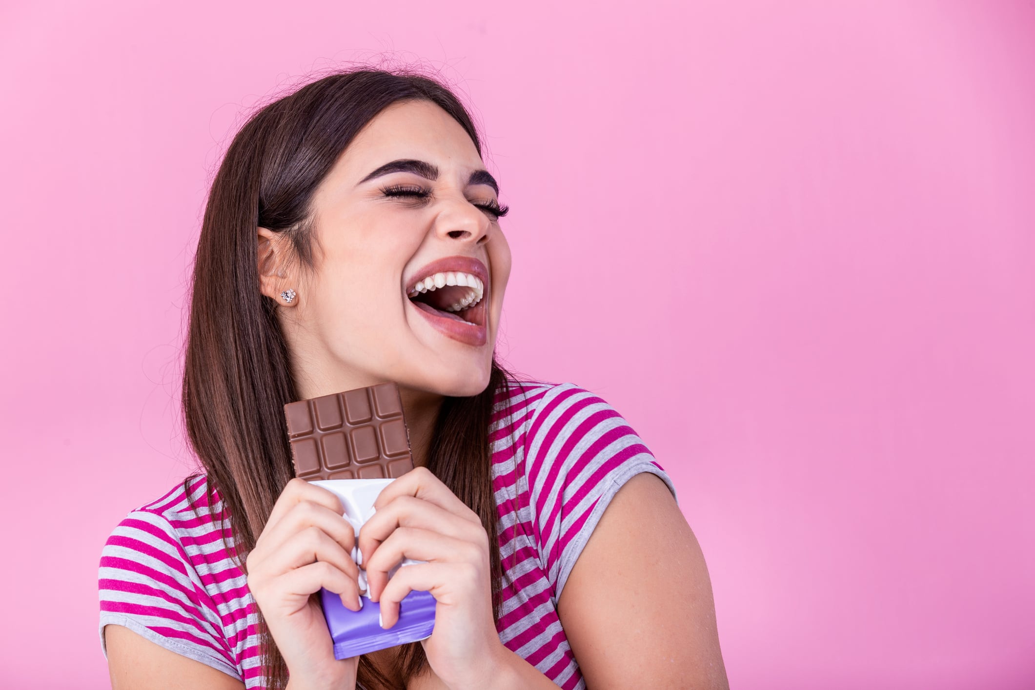 Woman holding bar of chocolate and smiling. Isolated on pink background.