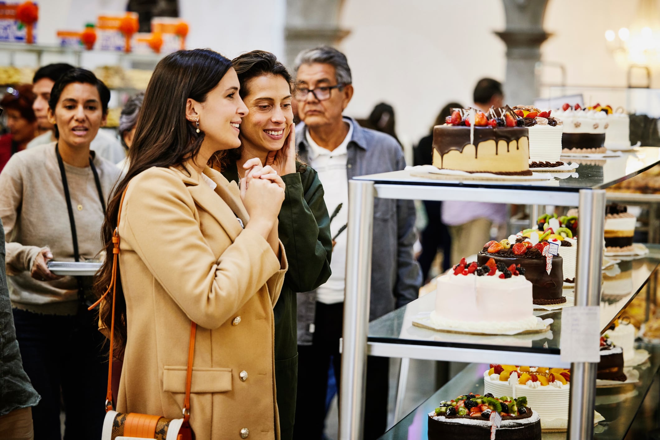 Medium wide shot of smiling friends admiring freshly made cakes while visiting bakery during city vacation