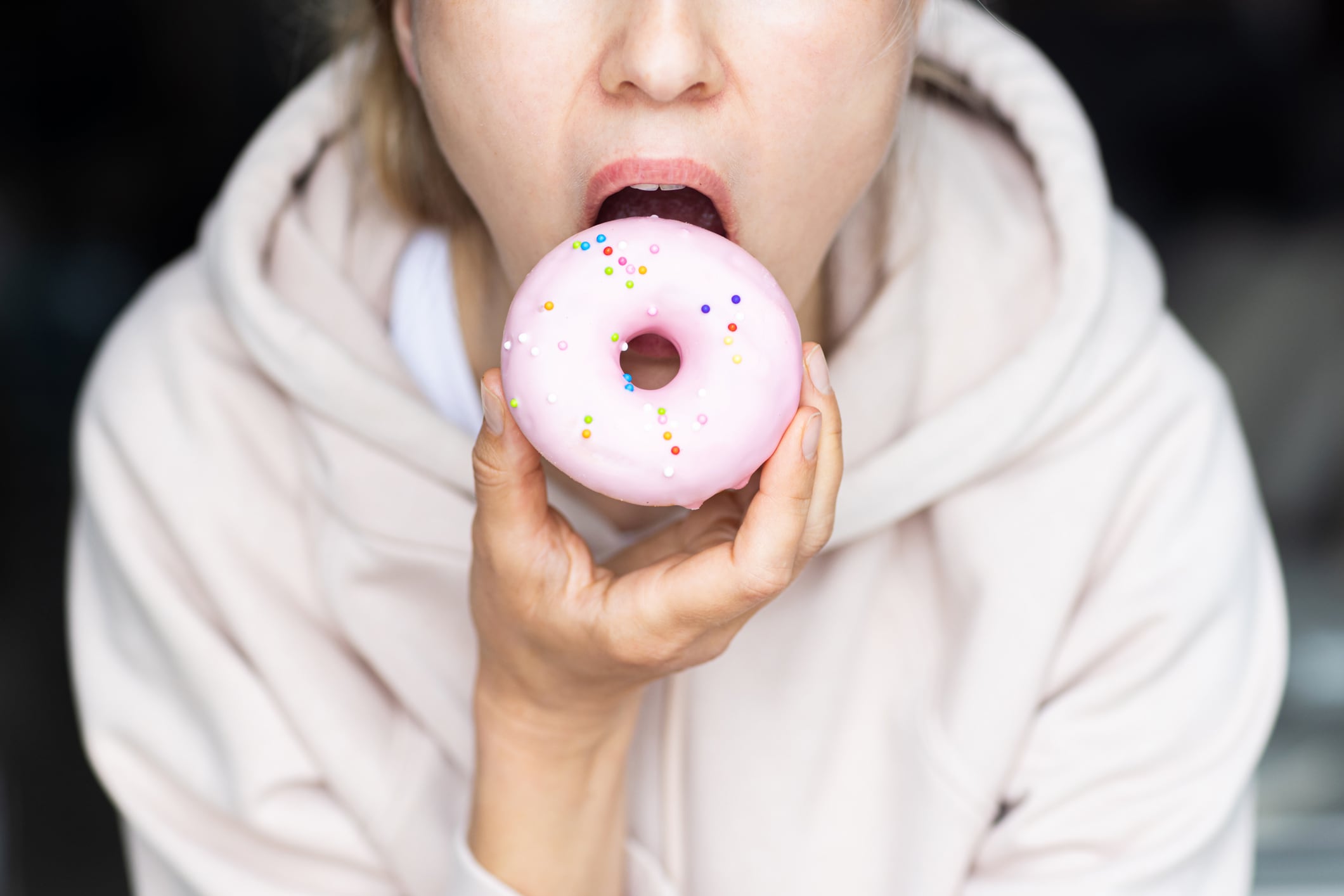 Unrecognizable young woman eating pink donut at home on kitchen. High quality photo