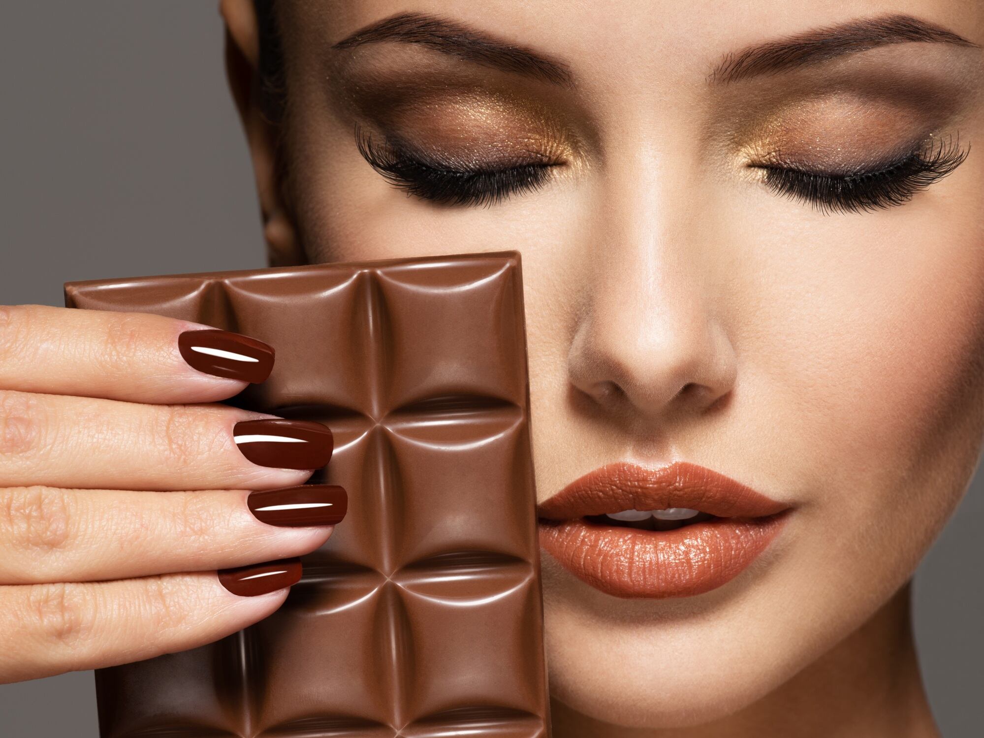 Woman with brown nails holding chocolate bar close to face.