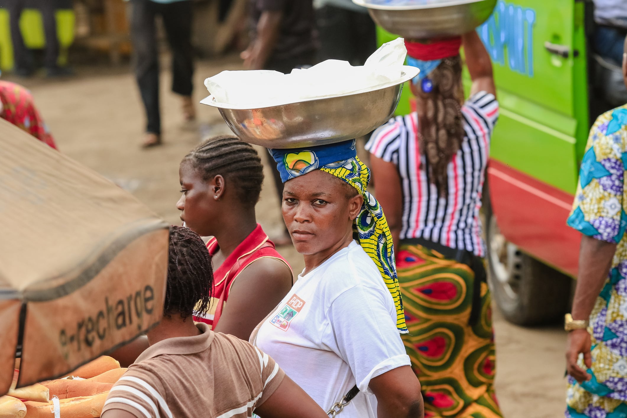 Yamoussoukro, Ivory Coast - November 16, 2024: Women engage in bustling market activities in Yamoussoukro while balancing goods on their heads amid vibrant surroundings.