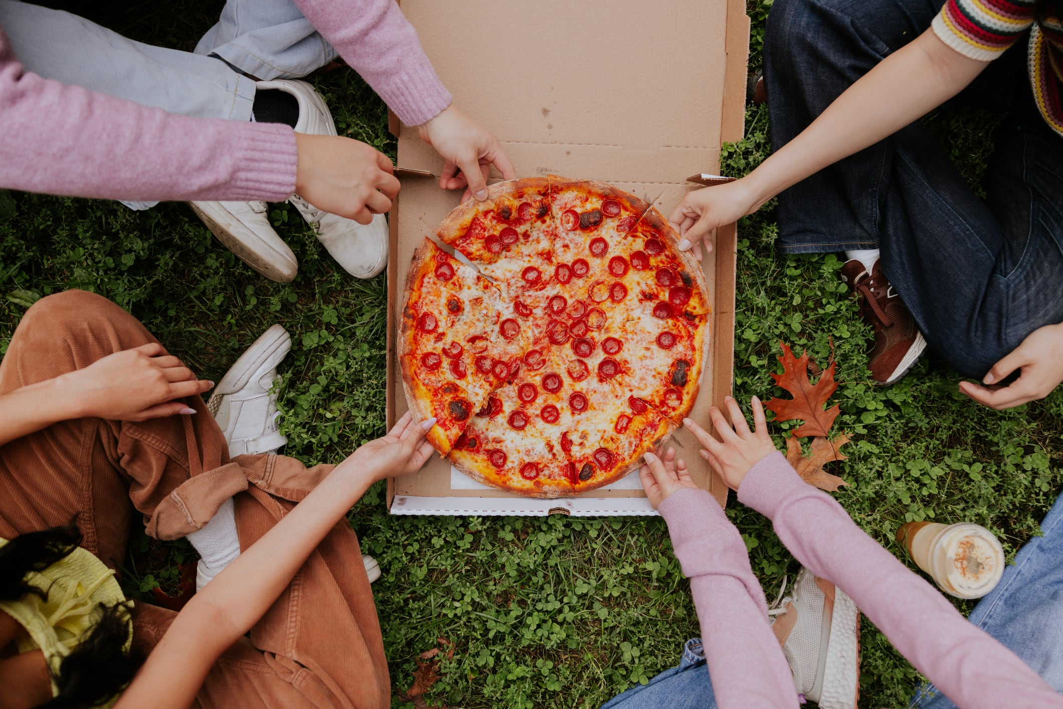 Surrounded by trees in Central Park Manhattan, these friends enjoy a moment of connection as one offers her pizza to the other, embodying the spirit of sharing good times.