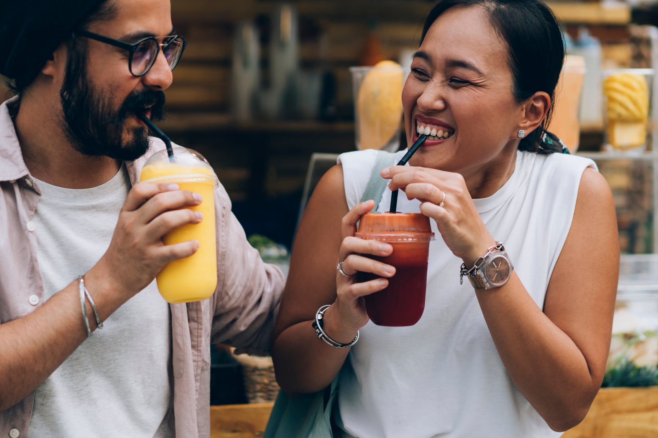 Two people laughing and smiling while drinking colourful smoothies.