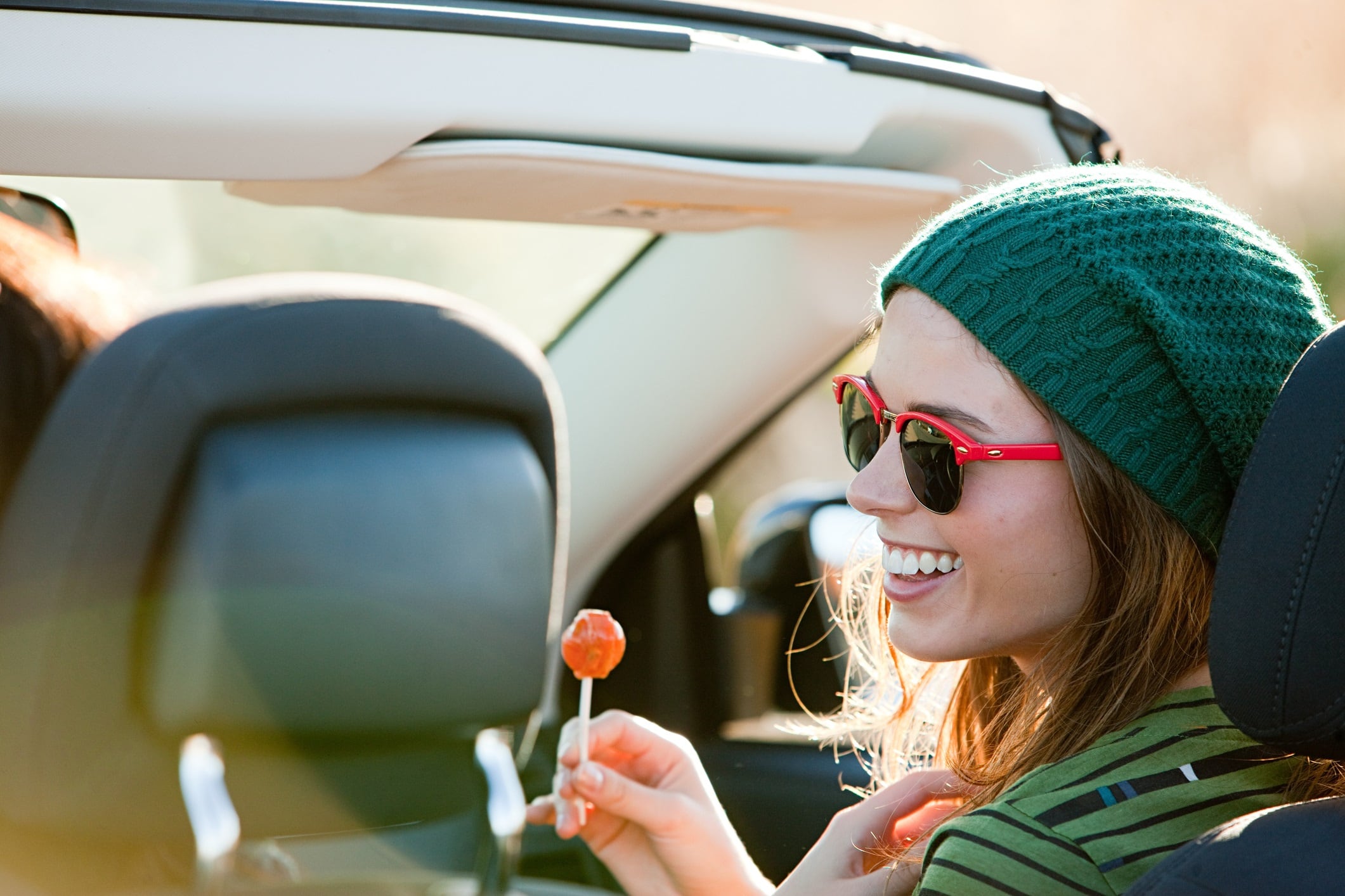 Woman in passenger seat of car, holding lollipop and smiling.