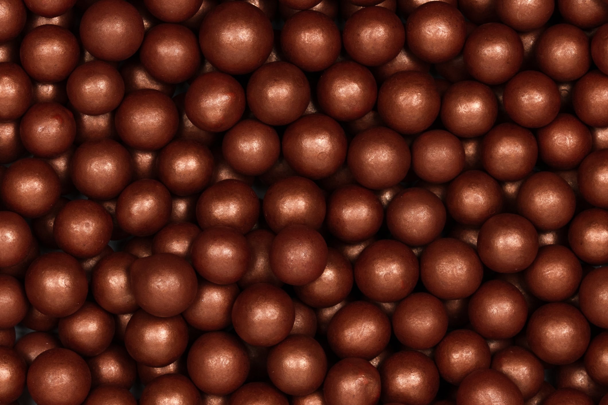 A close-up view of shiny bronze sugar pearls, commonly used as edible decorations for cakes, cupcakes, and other desserts. These metallic sprinkles add an elegant and festive touch to baked goods.