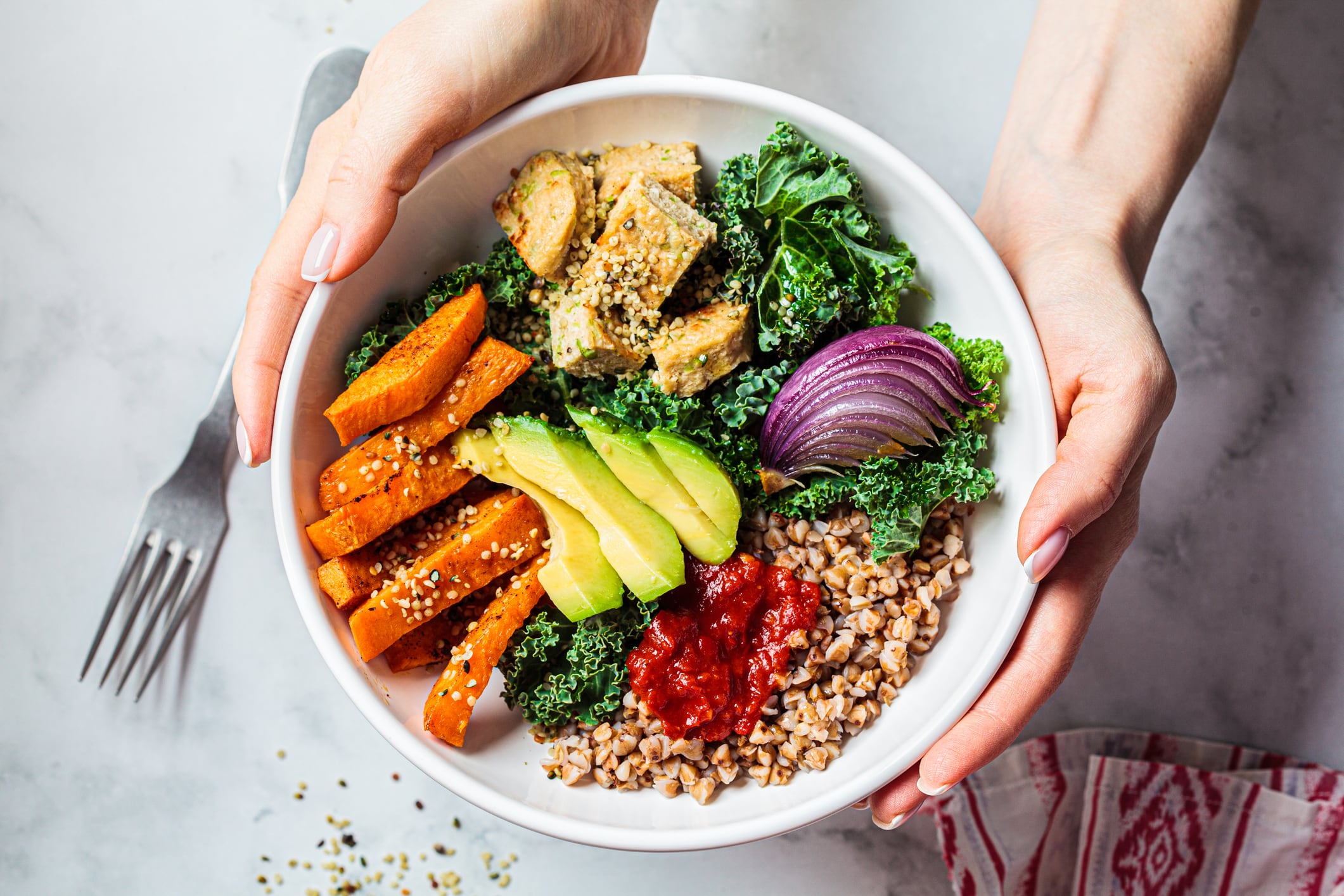 Woman's hands holding bowl of vegetables, avocado, tofu and buckwheat.