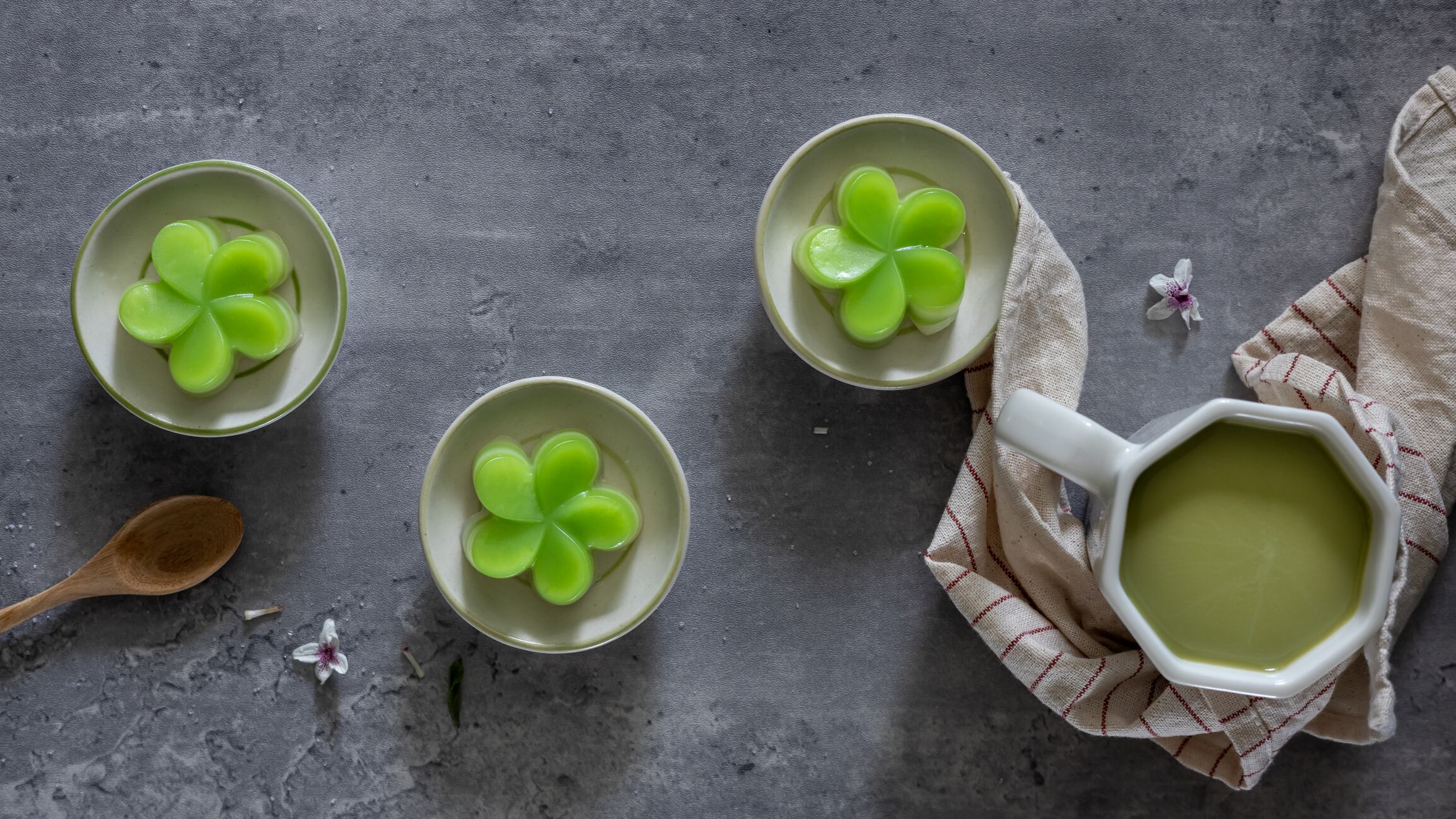 Top view of a steamed pandan layer cake on small cups, served with a cup of green tea, a traditional Thai dessert. Close-up. Flat lay.