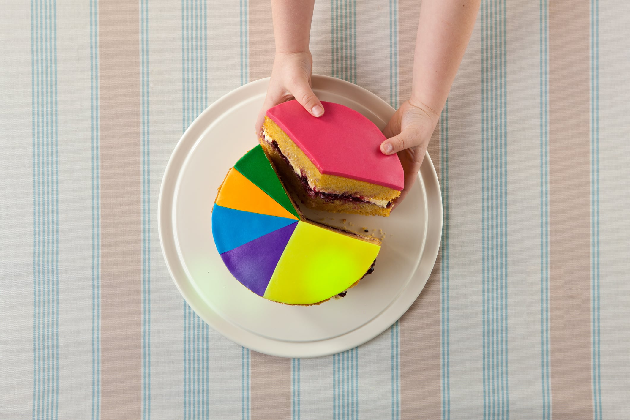 Aerial view of a 6 year old child's hands removing the largest slice of a sponge cake designed as a pie chart.