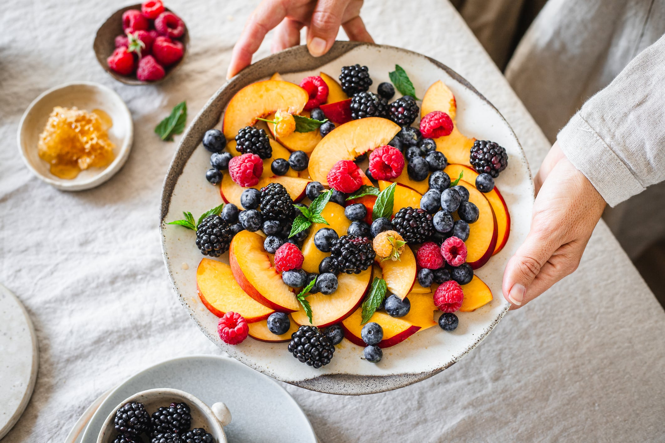 Close-up of a woman holding fresh fruit salad. Female hands serving healthy breakfast on table.