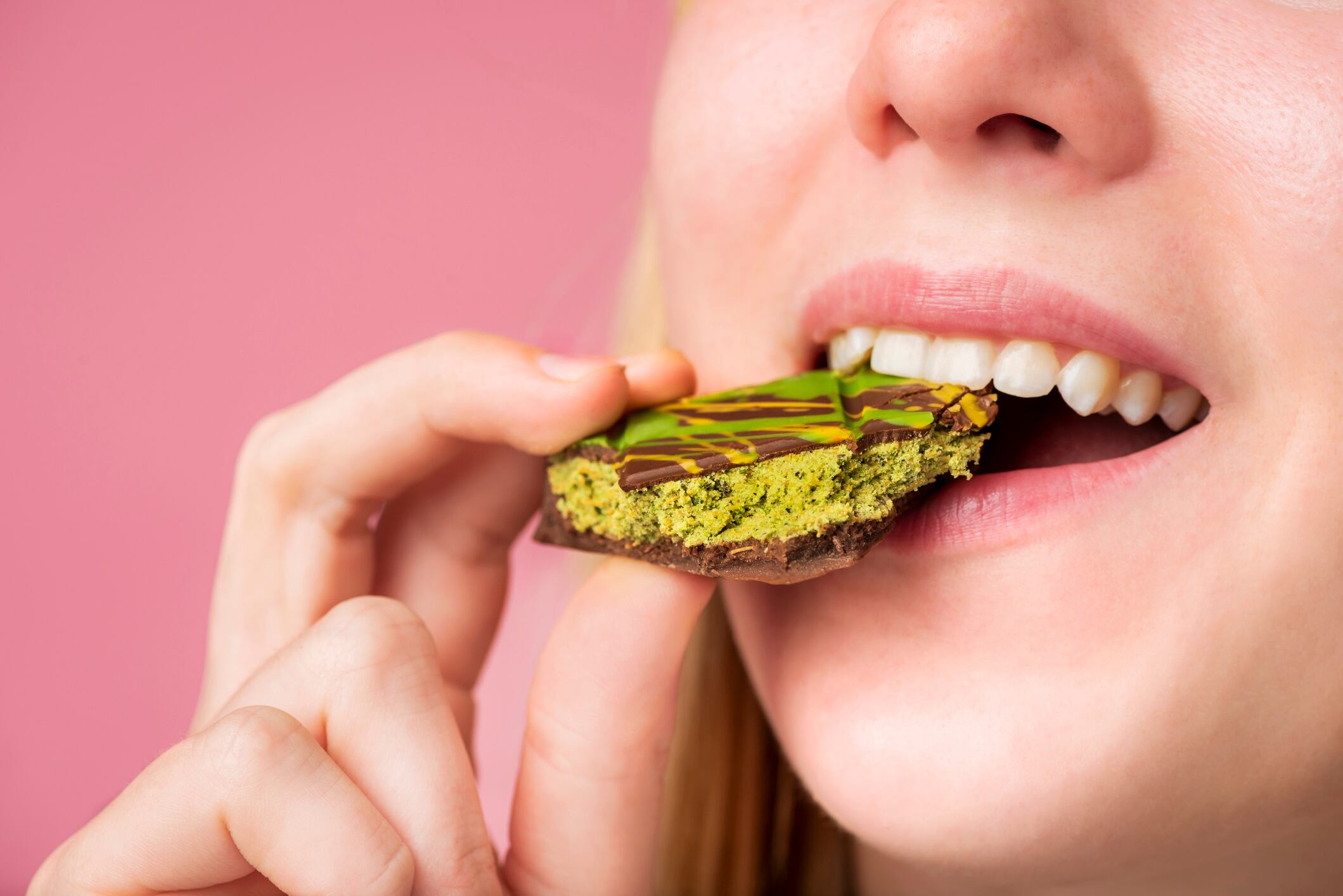 A young woman taking a bite from a bar of Dubai Chocolate revealing the filling made from pistachio cream, kataifi, and tahini. A shallow focus technique has been used to focus on the chocolate bar in the foreground.