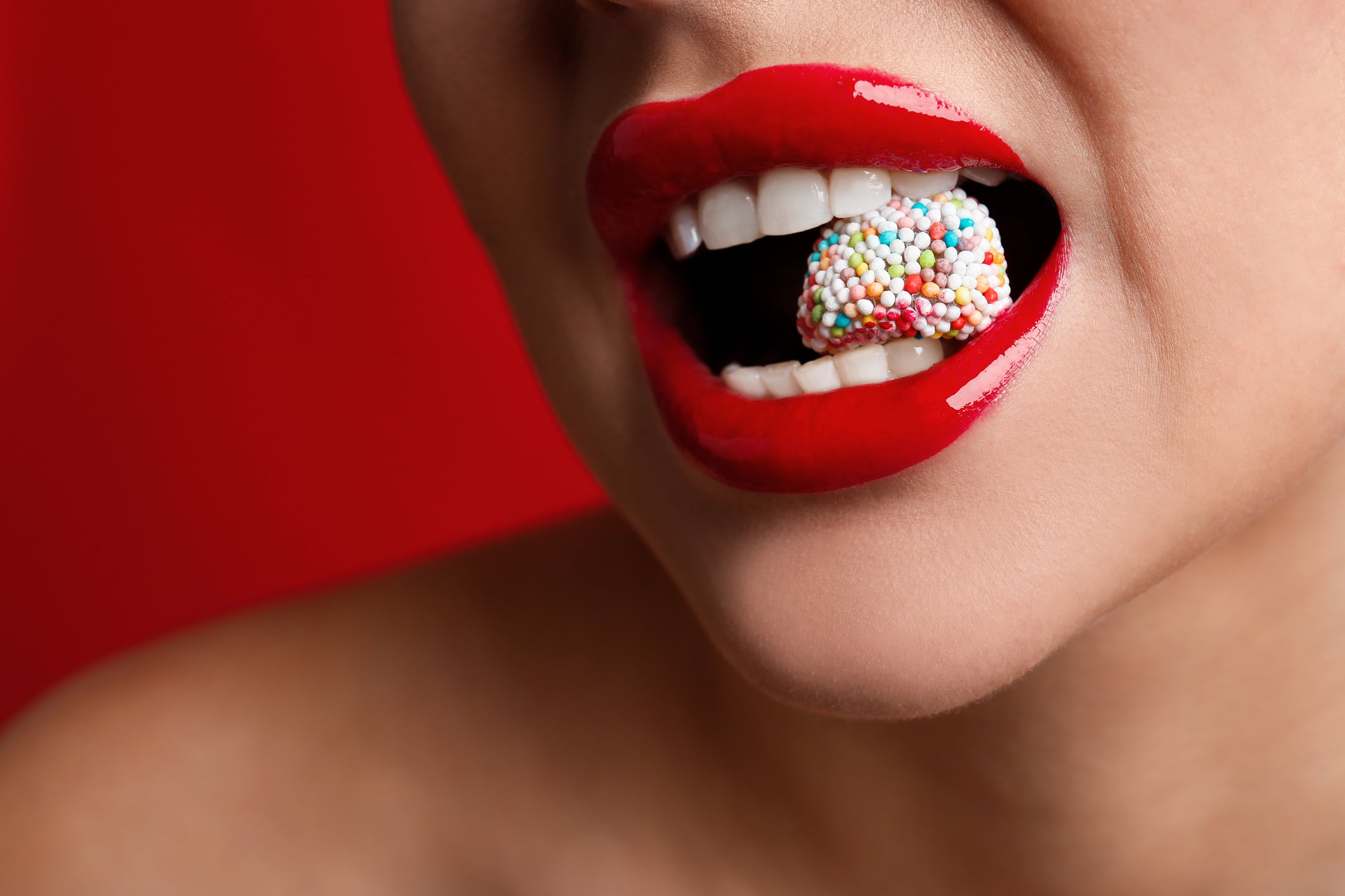 Closeup of woman with red lipstick, eating candy, on red background.