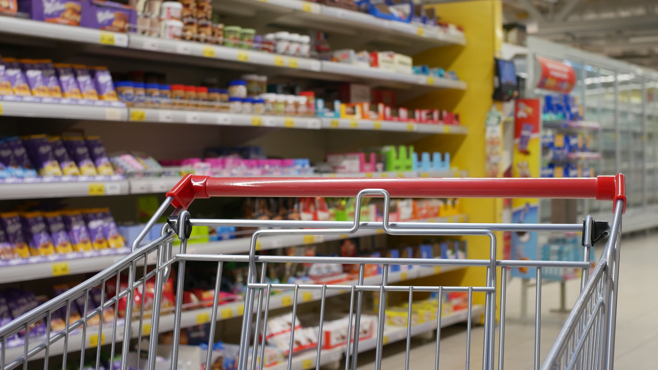 A metallic shopping trolley with a red handle in a shopping mall