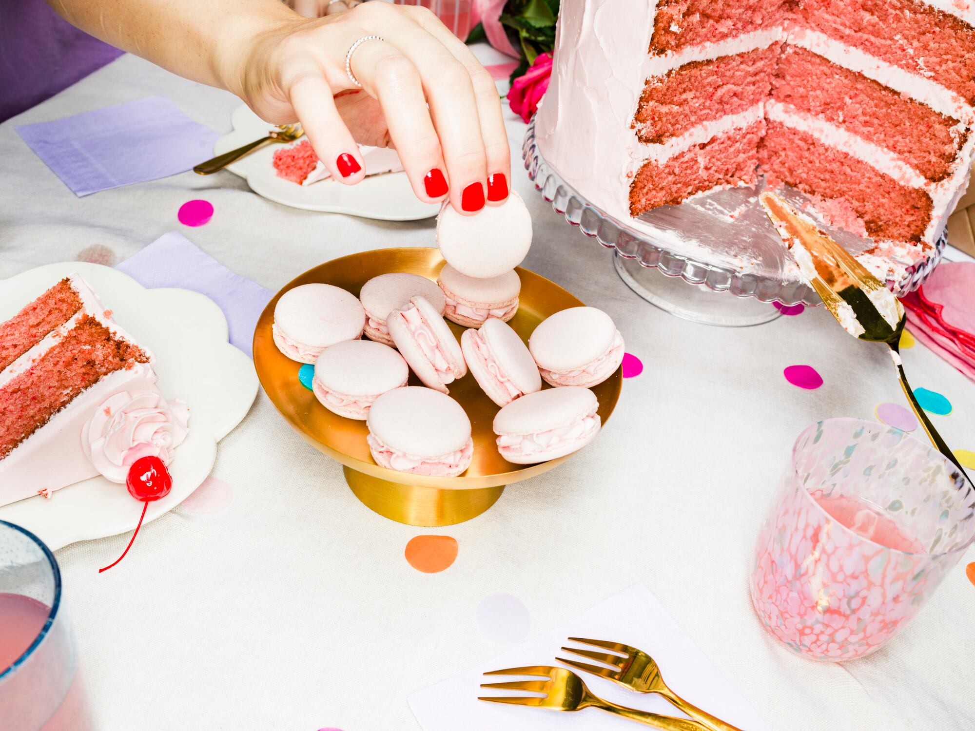 High Angle View Hand Of Woman Reaching For Pink Macaron Cookie Next To Birthday Cake On Table At Birthday Party