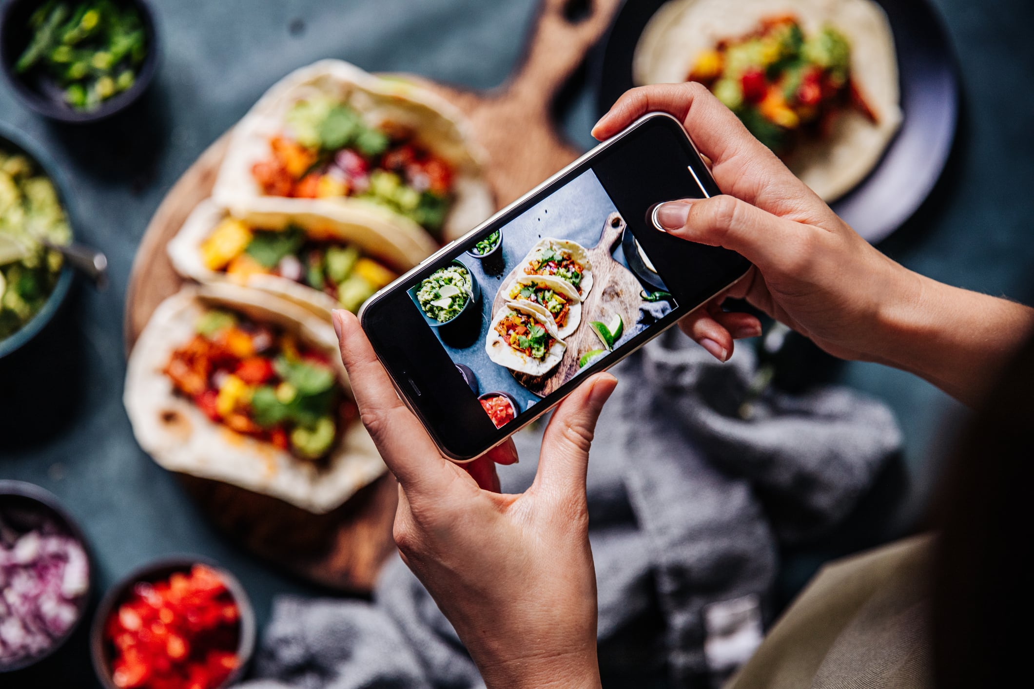 People search more for vegan than plant-based on social media and Google.
Image: Hand of a chef taking photograph of tacos on table with a mobile phone. Hands of cook photographing Mexican food .