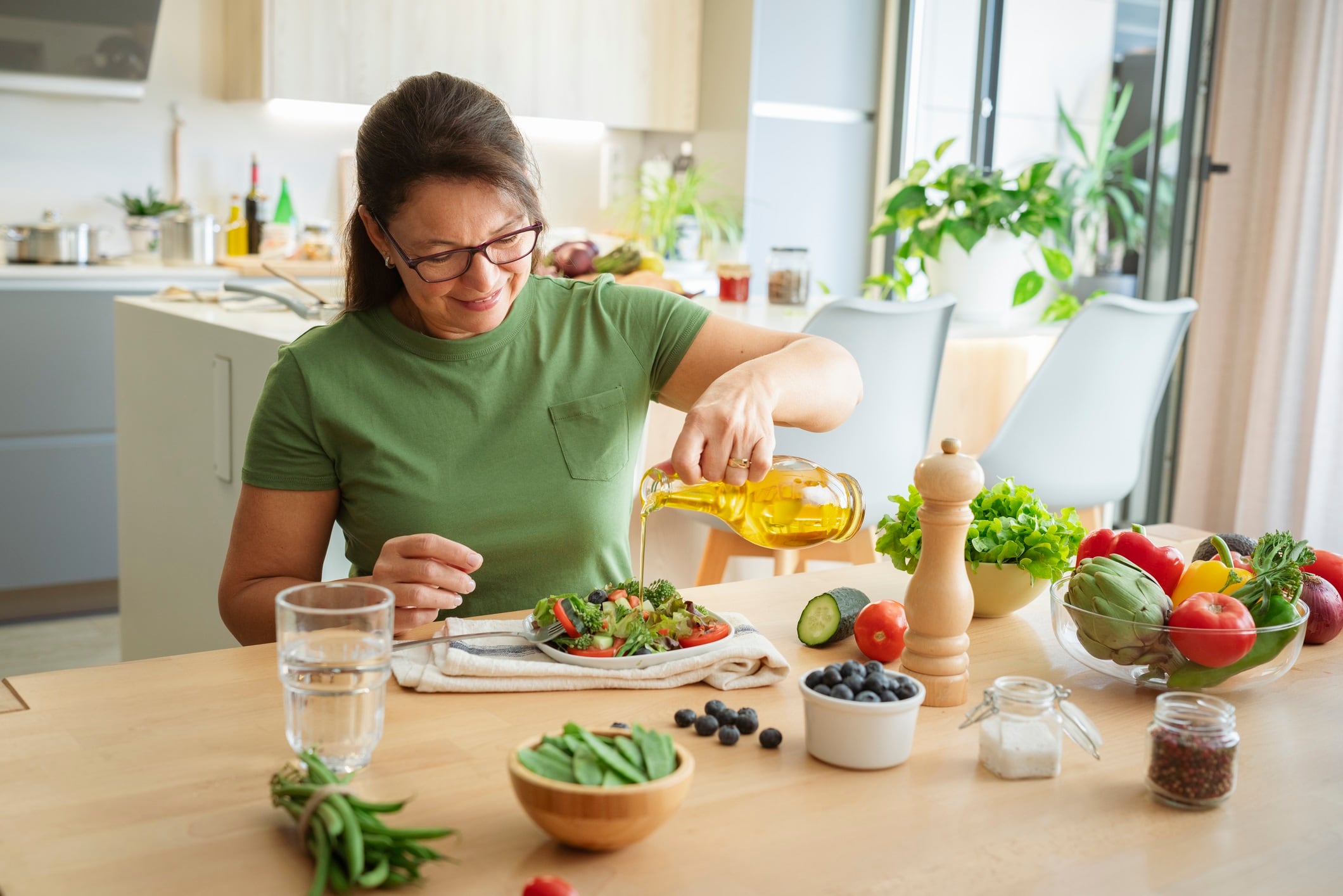 Woman sitting at the table dressing fresh organic vegetables salad plate with olive oil