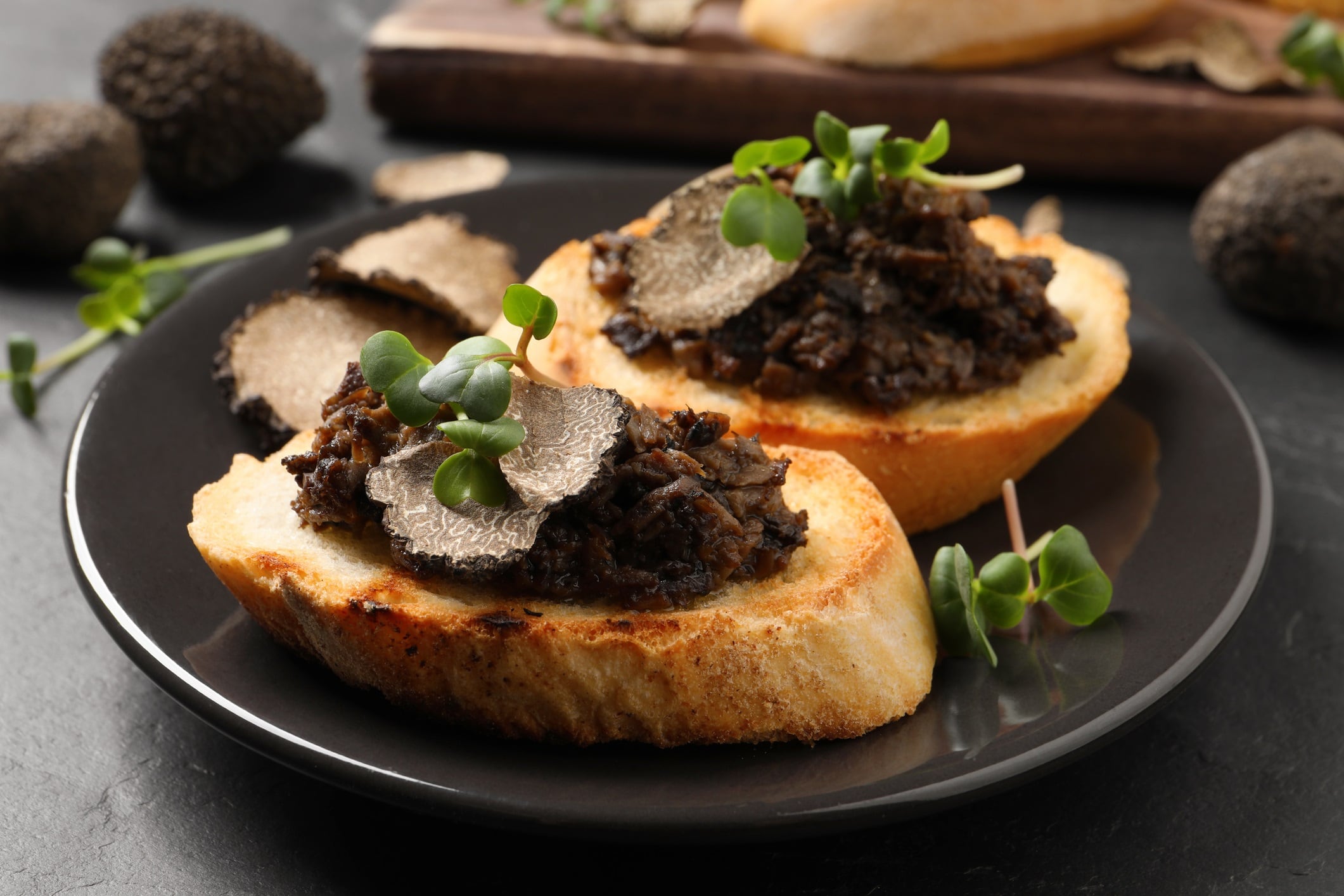 Delicious bruschettas with truffle sauce and microgreens on black table, closeup
