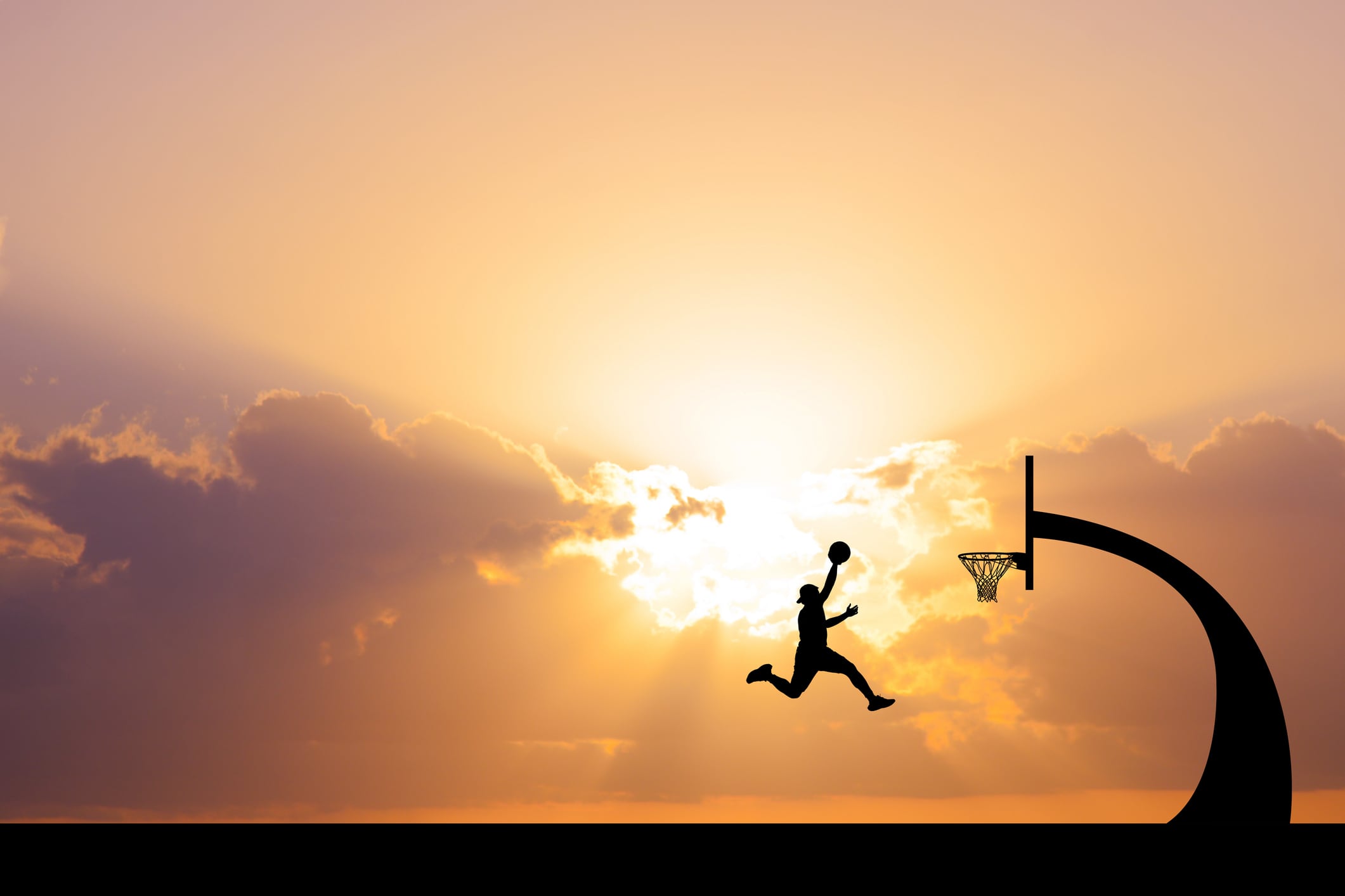 A dynamic silhouette of a basketball player mid-air, aiming for a dunk, with a stunning sunset backdrop.