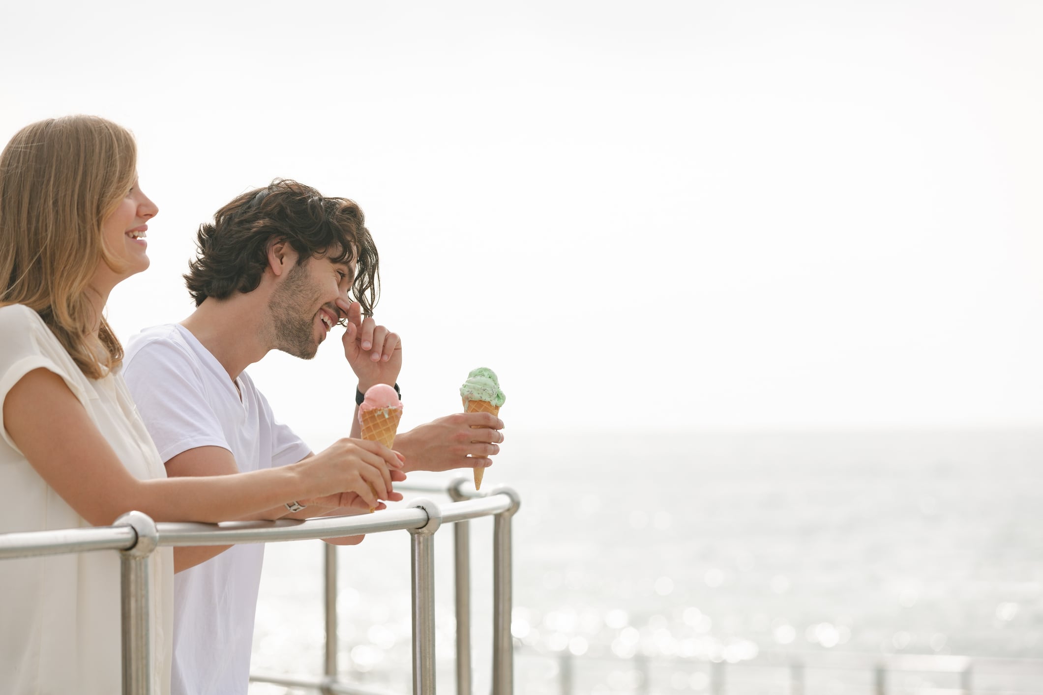 Side view of happy young couple standing at promenade while having ice cream cone. They are smiling