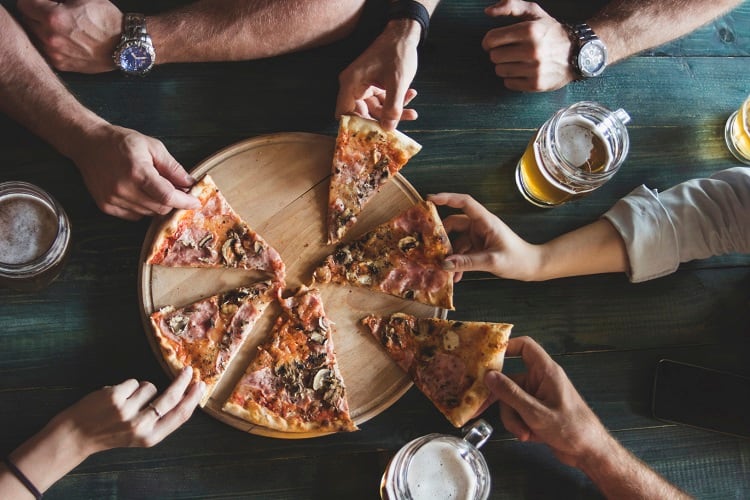 Hands reaching for pizza.