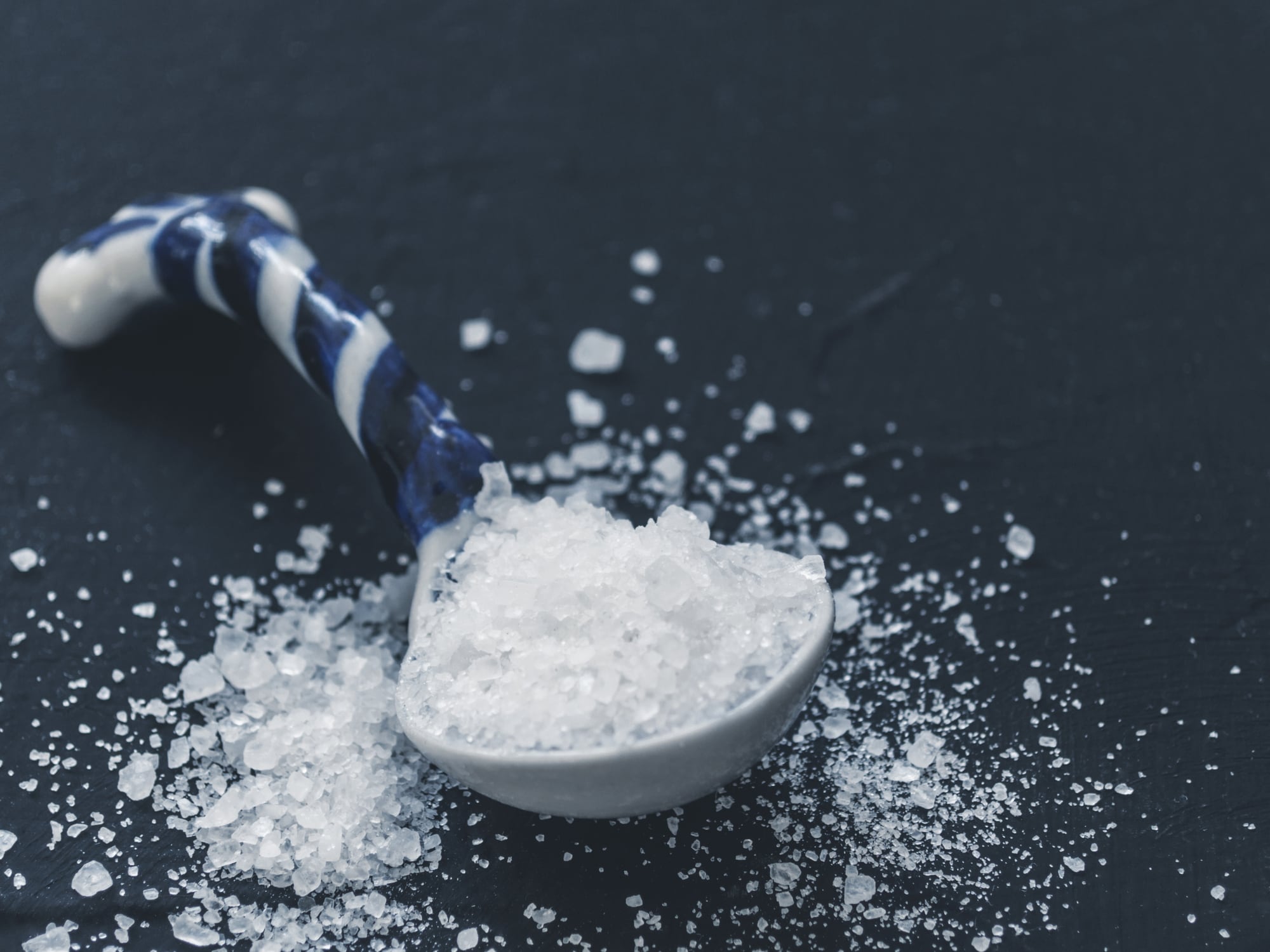White salt in spoon on black background