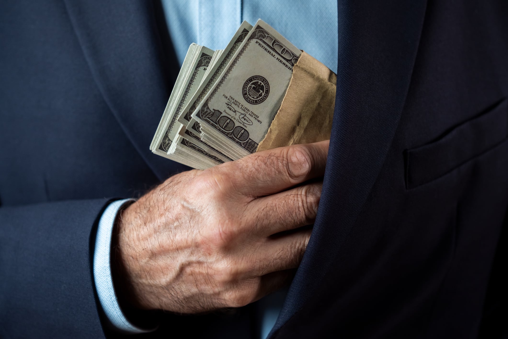 Man in Suit Concealing Cash in Envelope D-Keine GettyImages-2190411342.jpg
