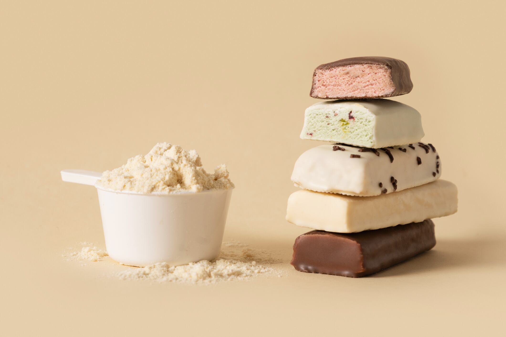 Whey protein bars with various chocolate coatings and sprinkles scoop of protein powder on beige background. Healthy fitness snacks.