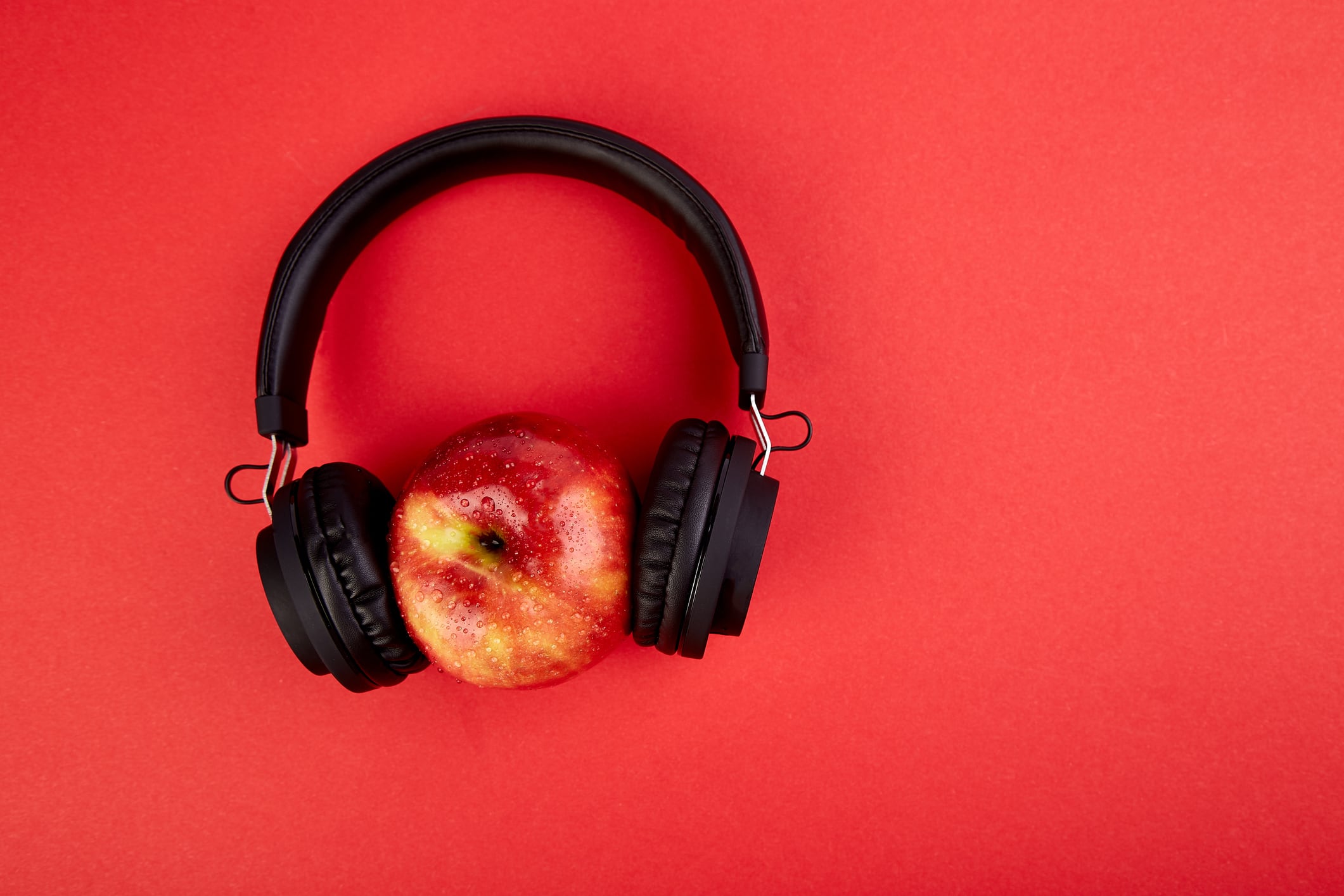 Black Headphones and apple  on red background. Flat lay. Top view. Copy space.