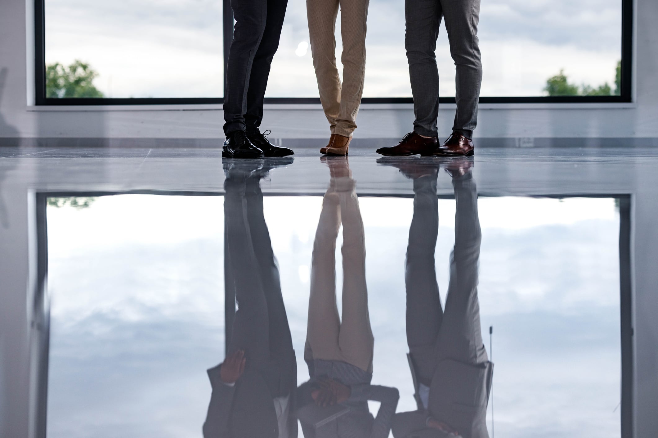 Group of unrecognizable business people standing on a floor in the office. In a reflection is seen that two of them are shaking hands. Copy space.