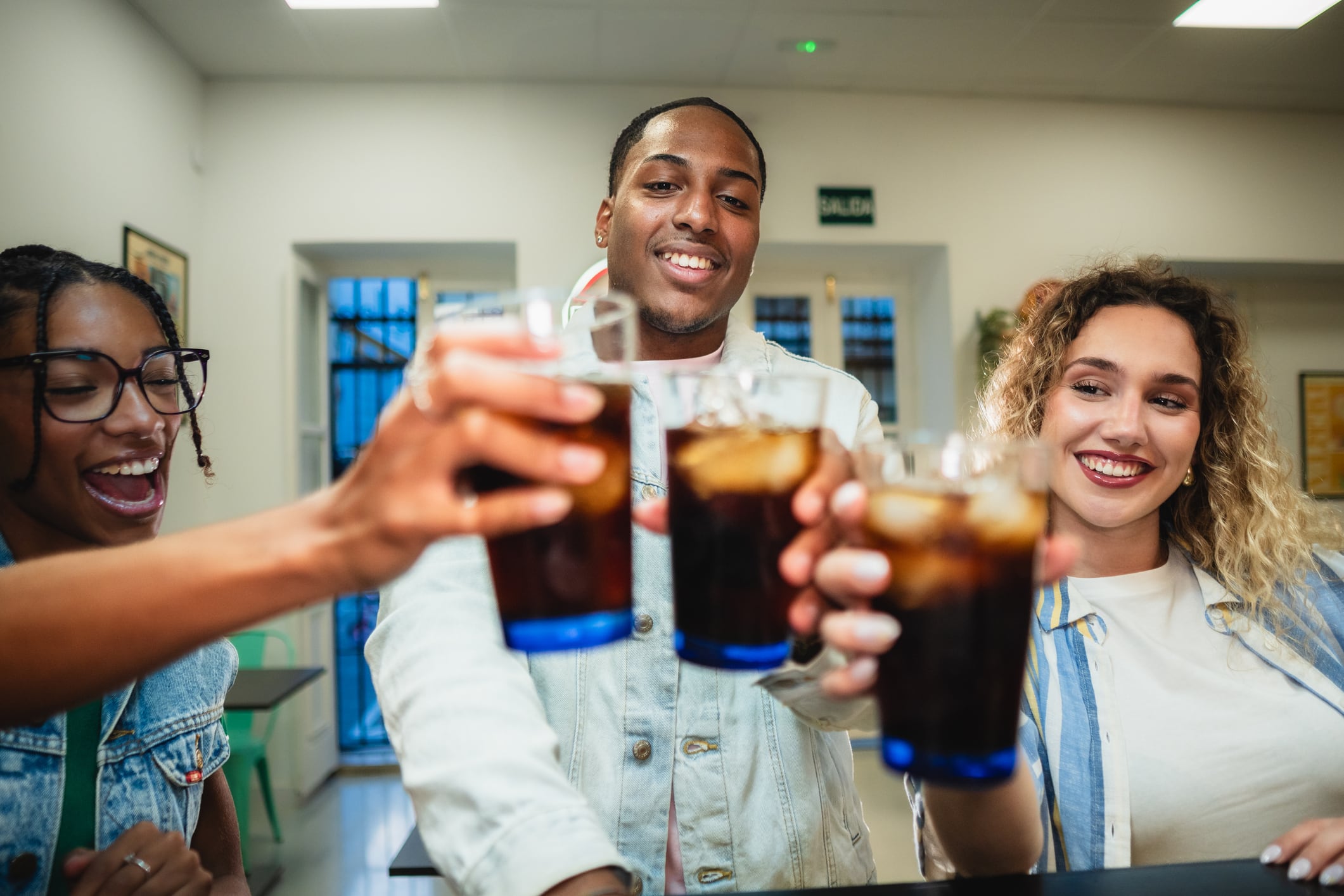 Three diverse friends cheering with soft drink glasses, celebrating friendship and good times