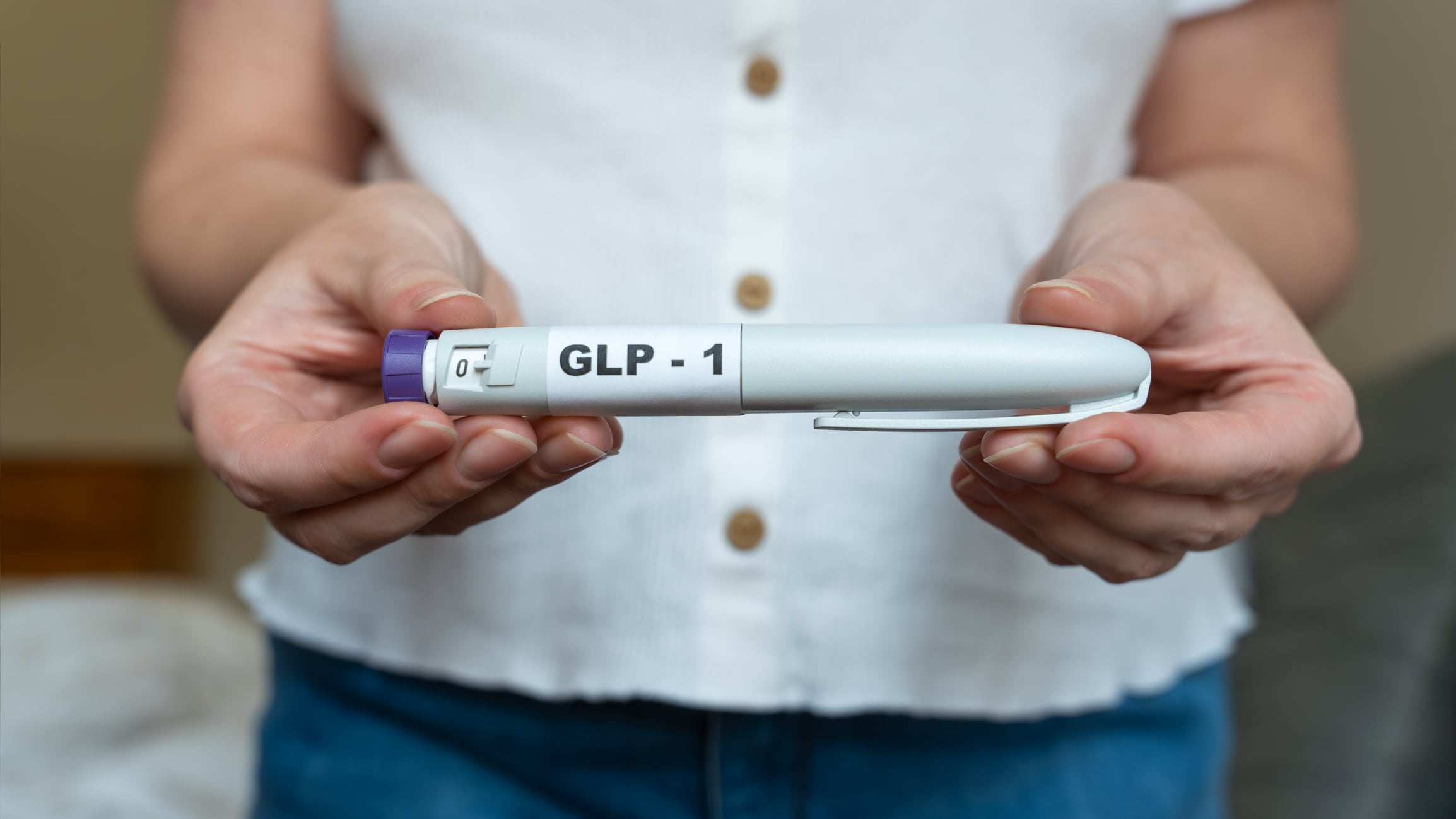 Close-up of a woman holding a GLP-1 injection pen in both hands with her bare abdomen visible in the background. The image illustrates weight management, hormone therapy, modern medical treatment, and body changes related to GLP-1 medications.