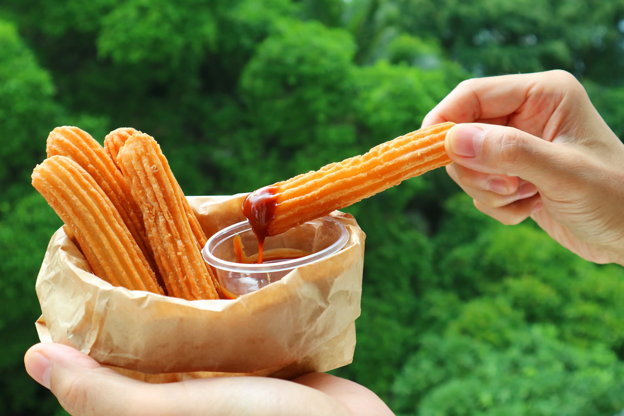 Hand Dipping a Stick of Churro in Dolce de Leche Caramel Sauce