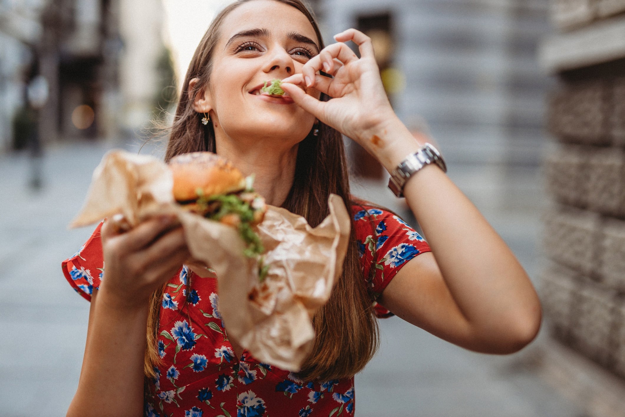 Woman wearing red patterned dress and eating burger.