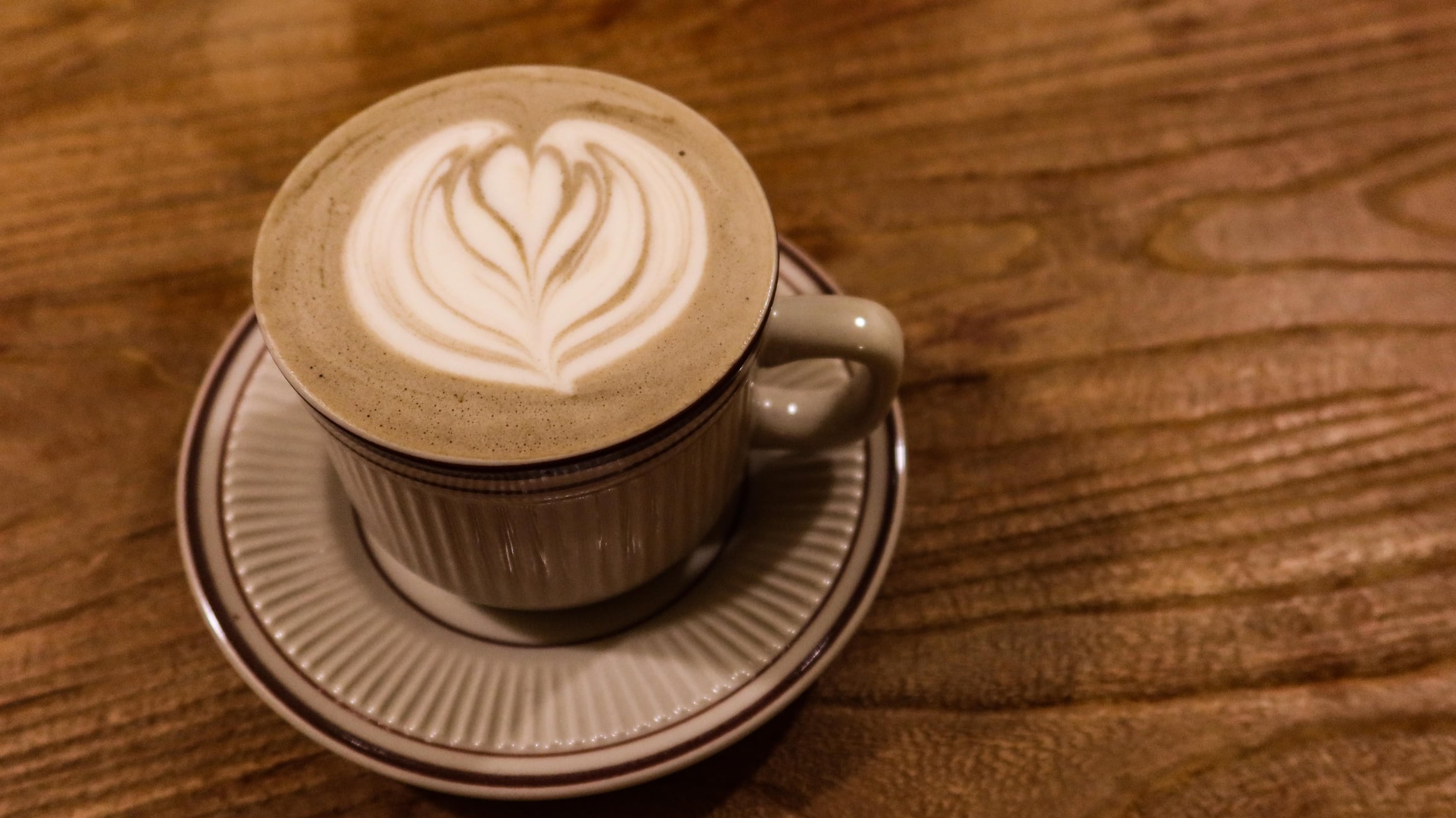 Hojicha latte with coffee art and foam on top in a mug.