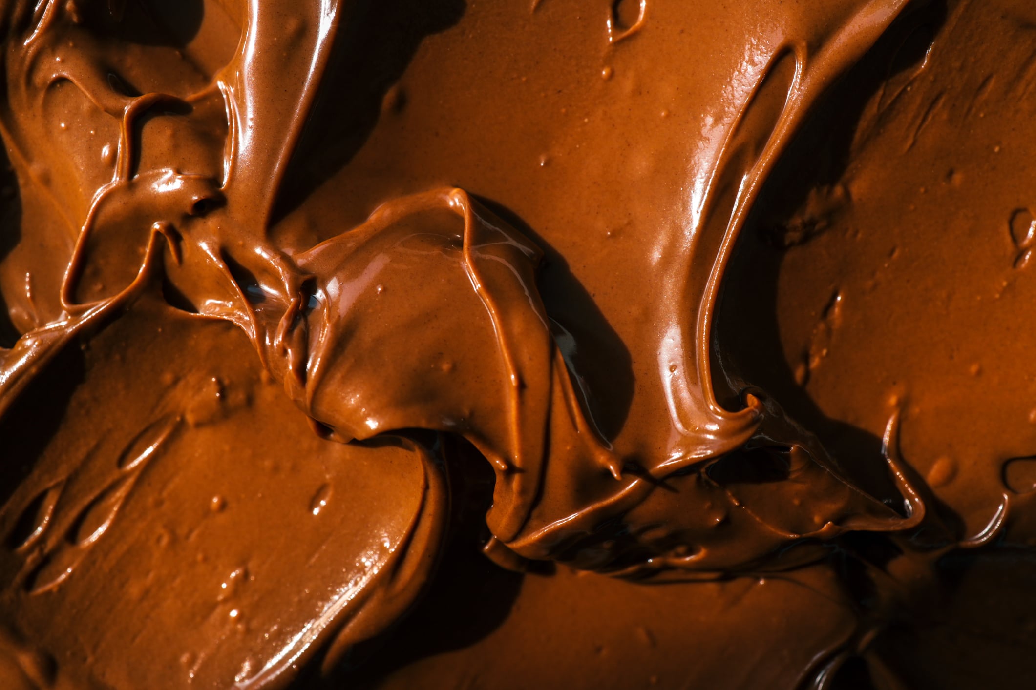 Close-up of smooth chocolate frosting with rich texture and deep brown color. The creamy, glossy surface has distinct swirls, highlighting its velvety consistency, perfect for cakes and desserts.