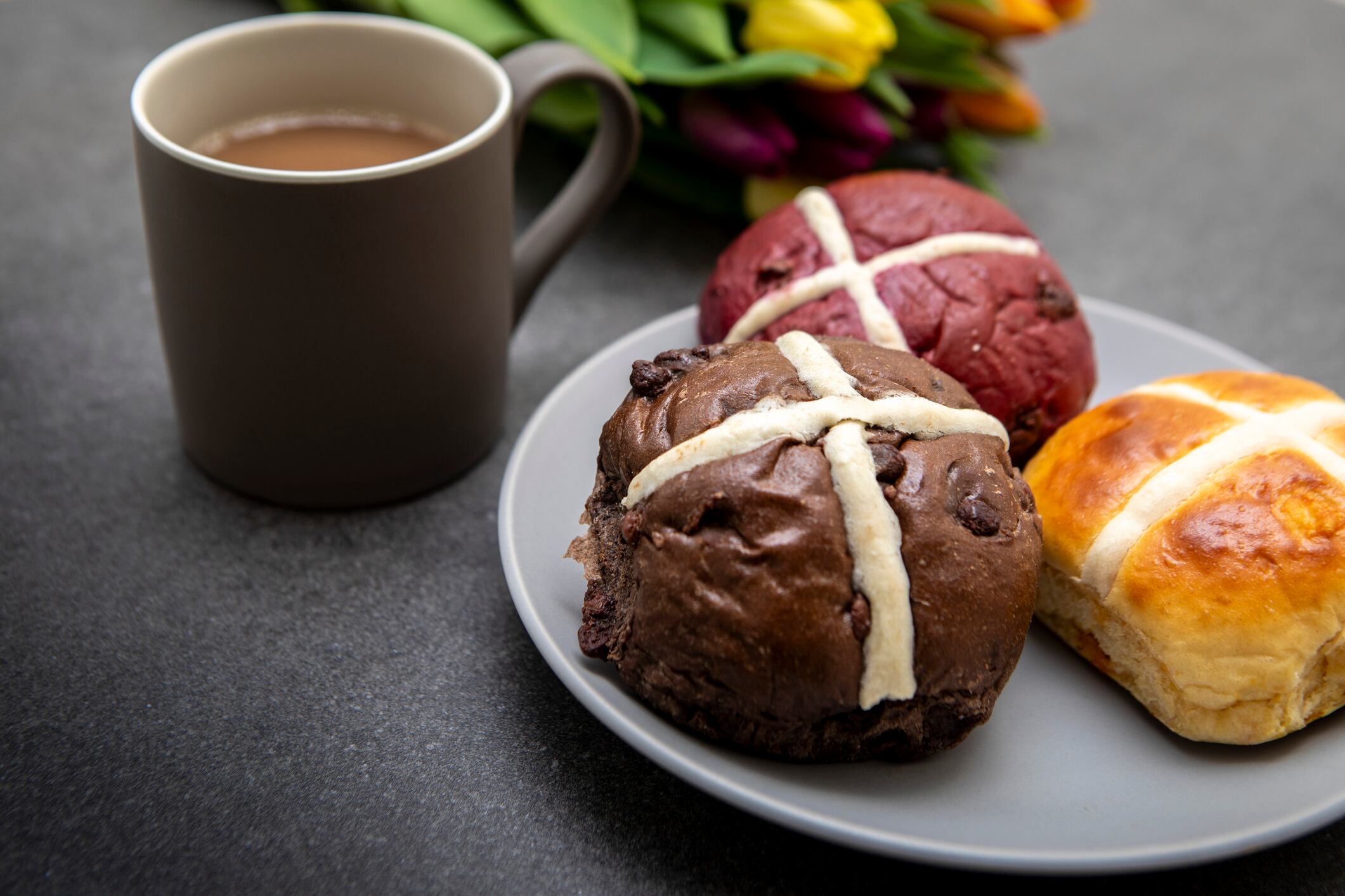 Unconventional hot cross bun recipes: Cheese, Chocolate & Red Velvet Cake. Photographed on a dark grey slate surface with grey-coloured crockery.