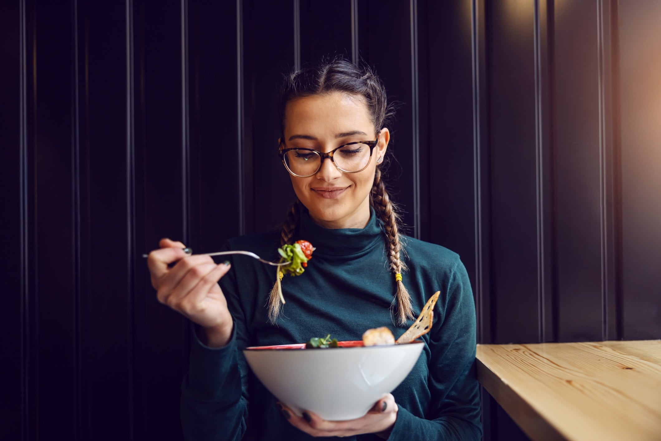 Young attractive teenage girl with healthy habits sitting in restaurant, holding bowl with salad and having lunch.