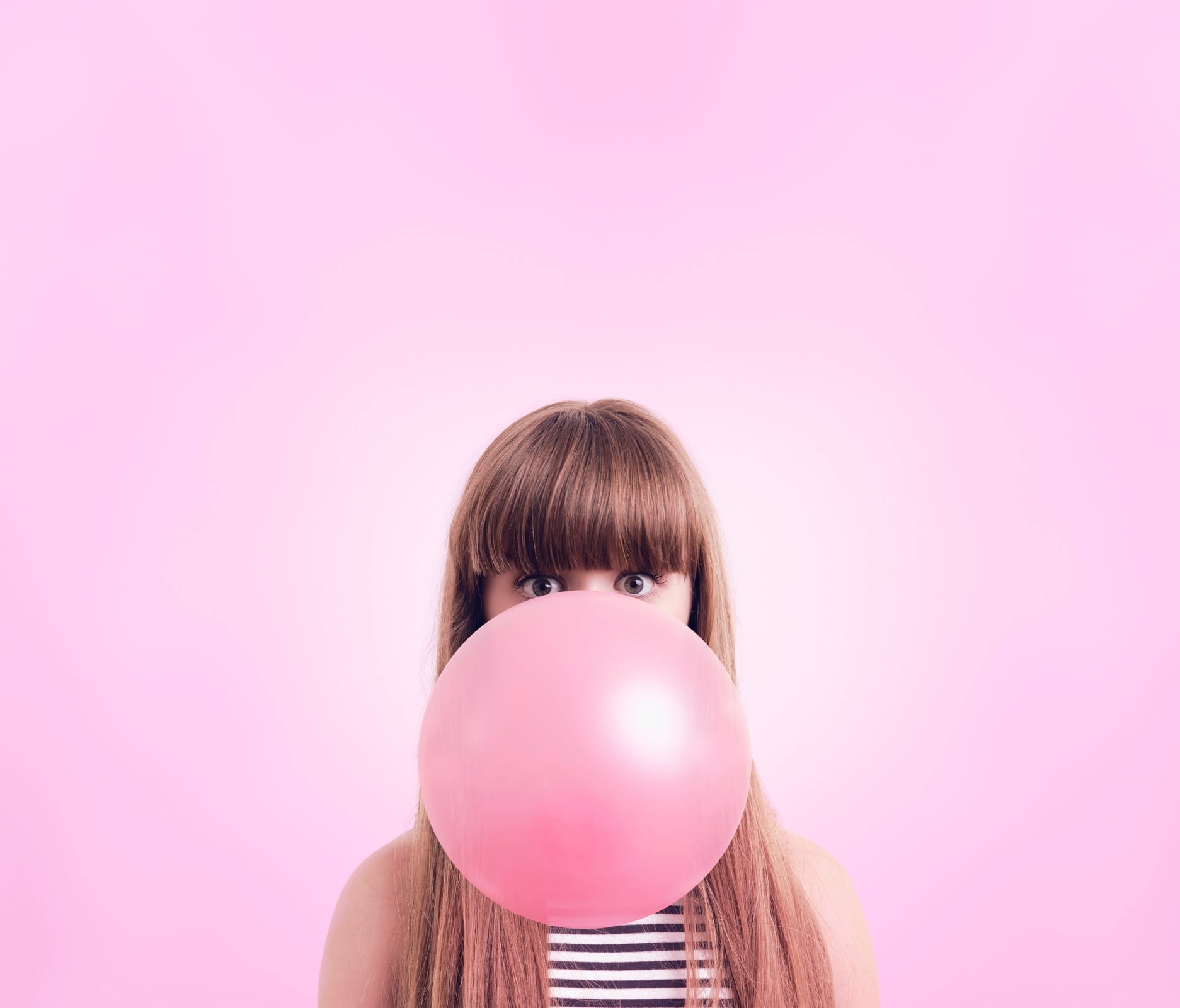 Woman blowing large pink bubble in bubblegum. Pink background.