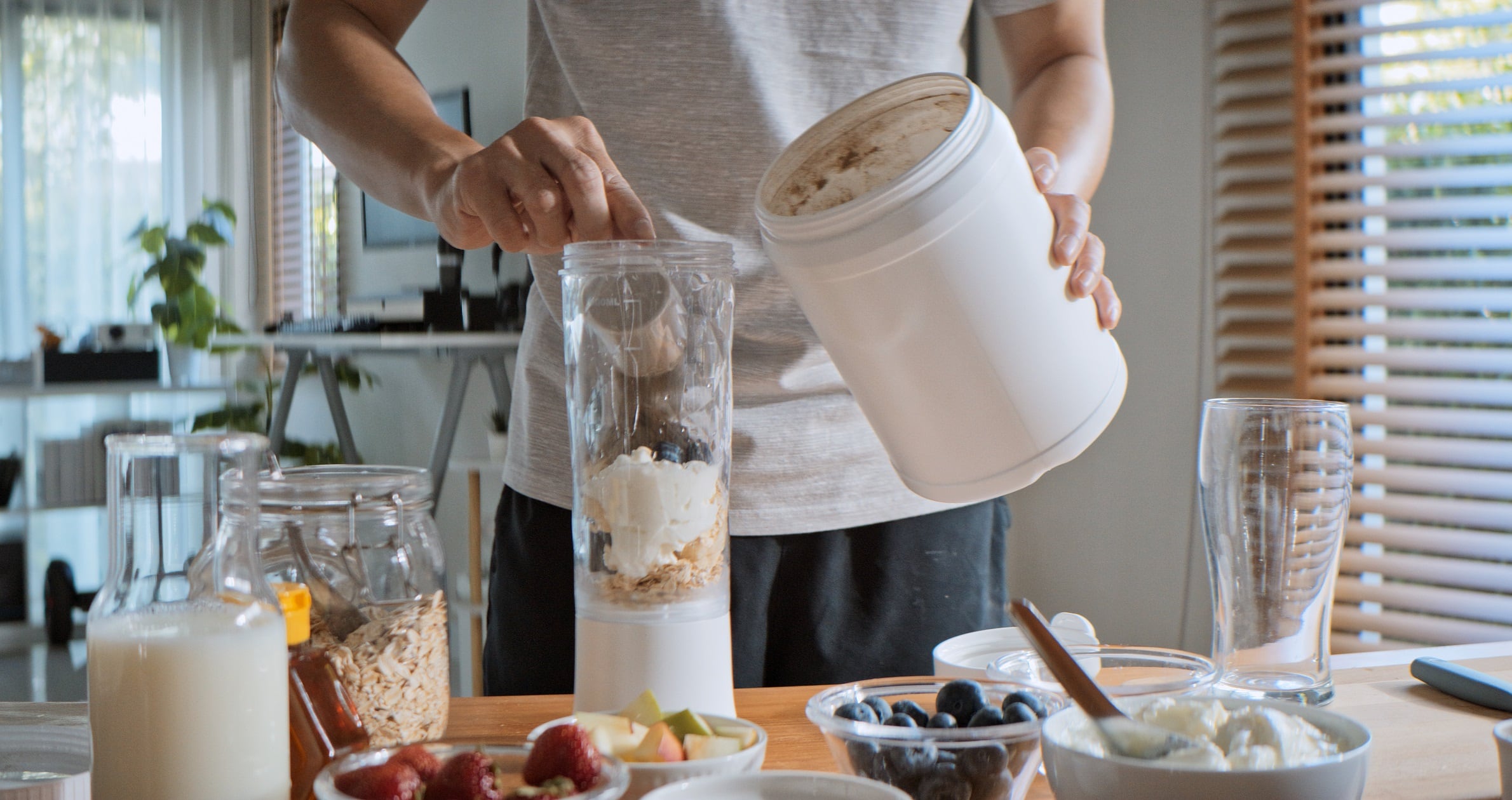 Adult man prepares protein shake using blender.