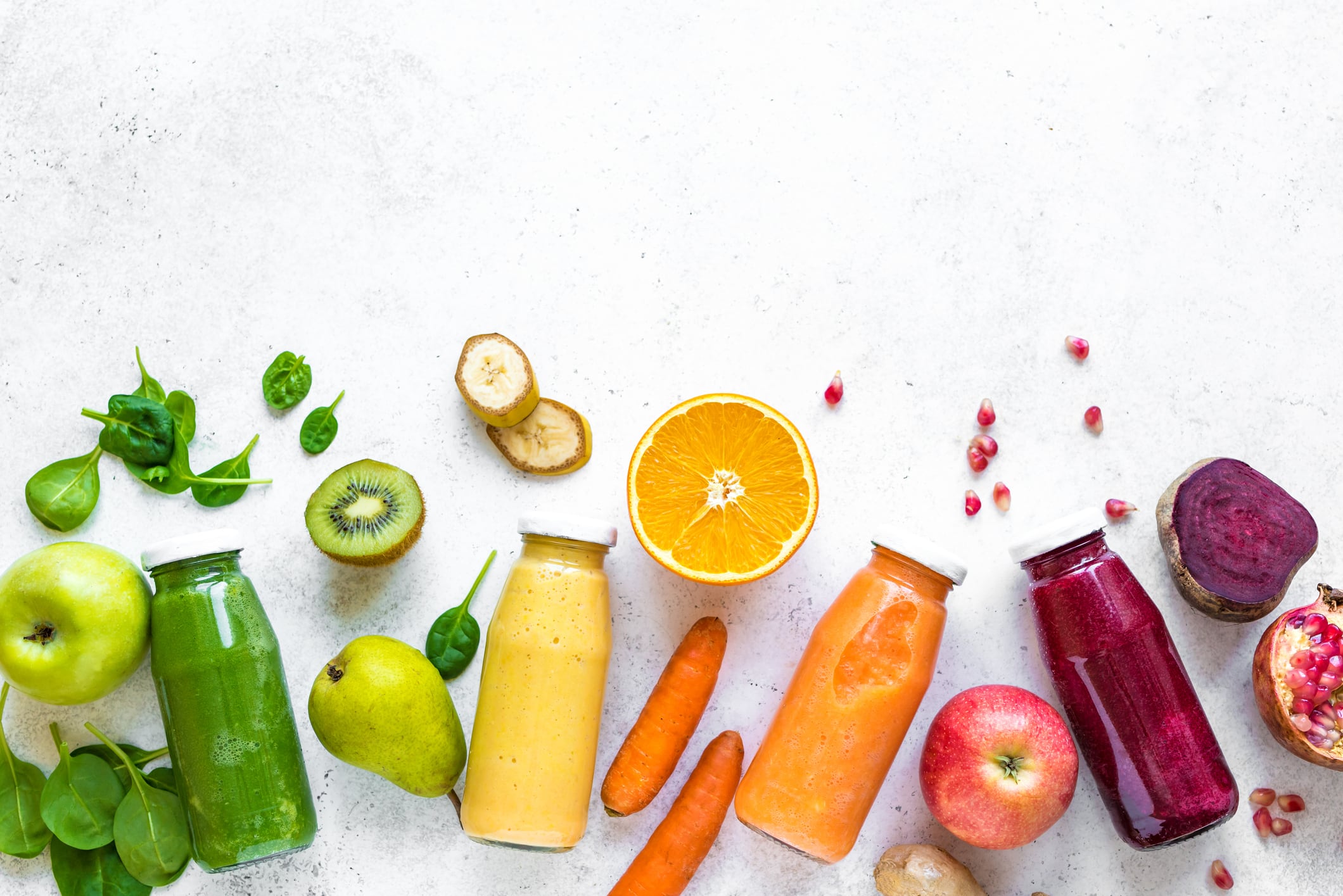 Various smoothies or juices in bottles and ingredients on white, healthy diet detox vegan clean food concept, top view, copy space.