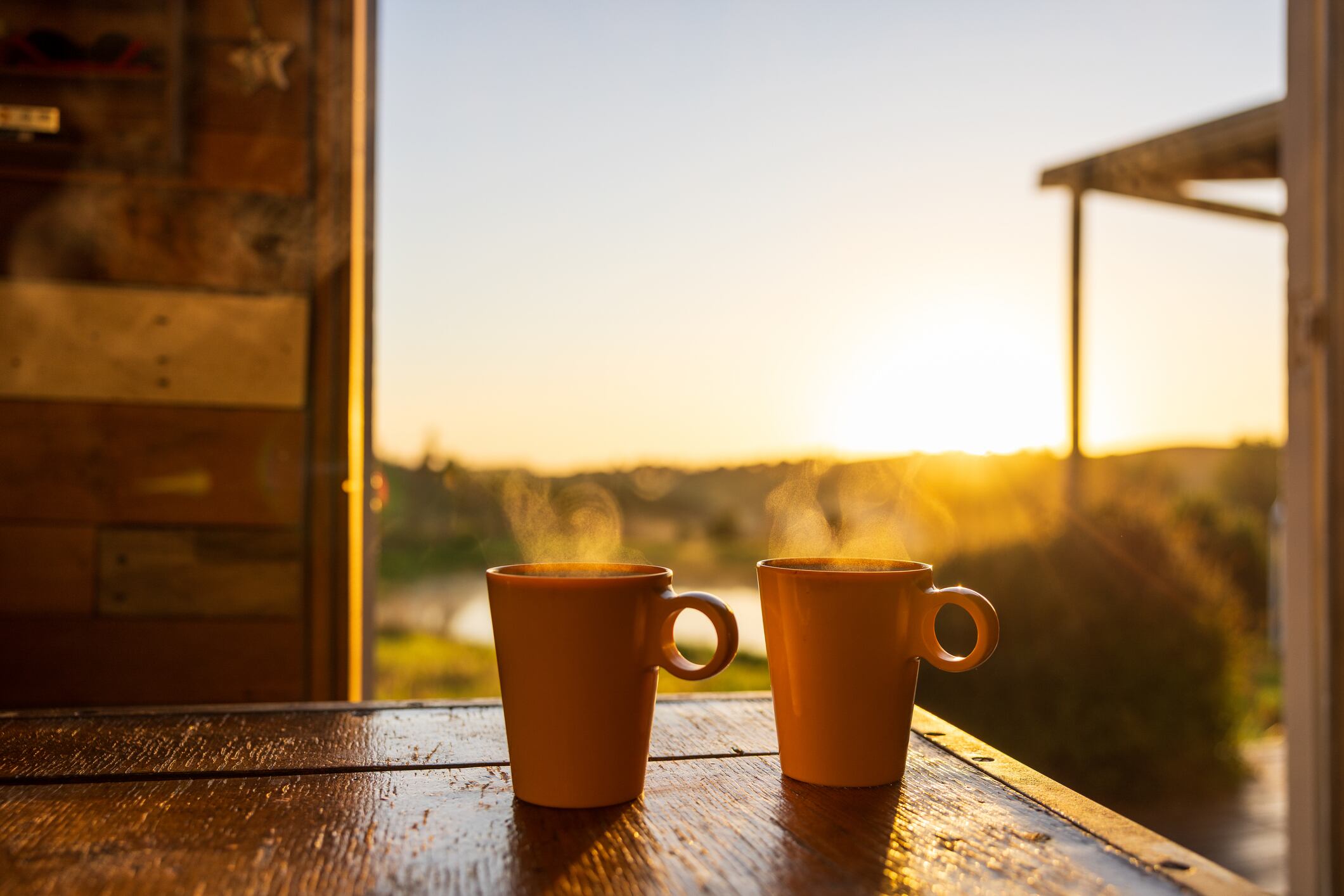 Two cups of coffee with the sunrise behind them