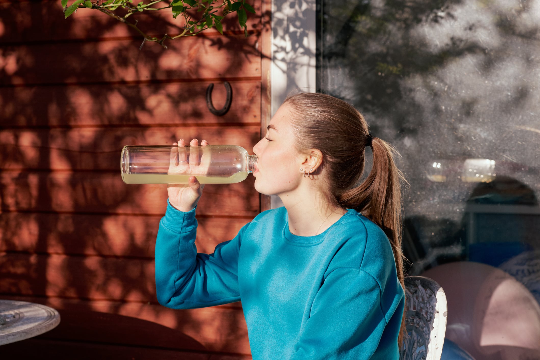 UK, Harlow, Essex, young woman sitting drinking water from a reusable bottle after practicing yoga in her garden in springtime