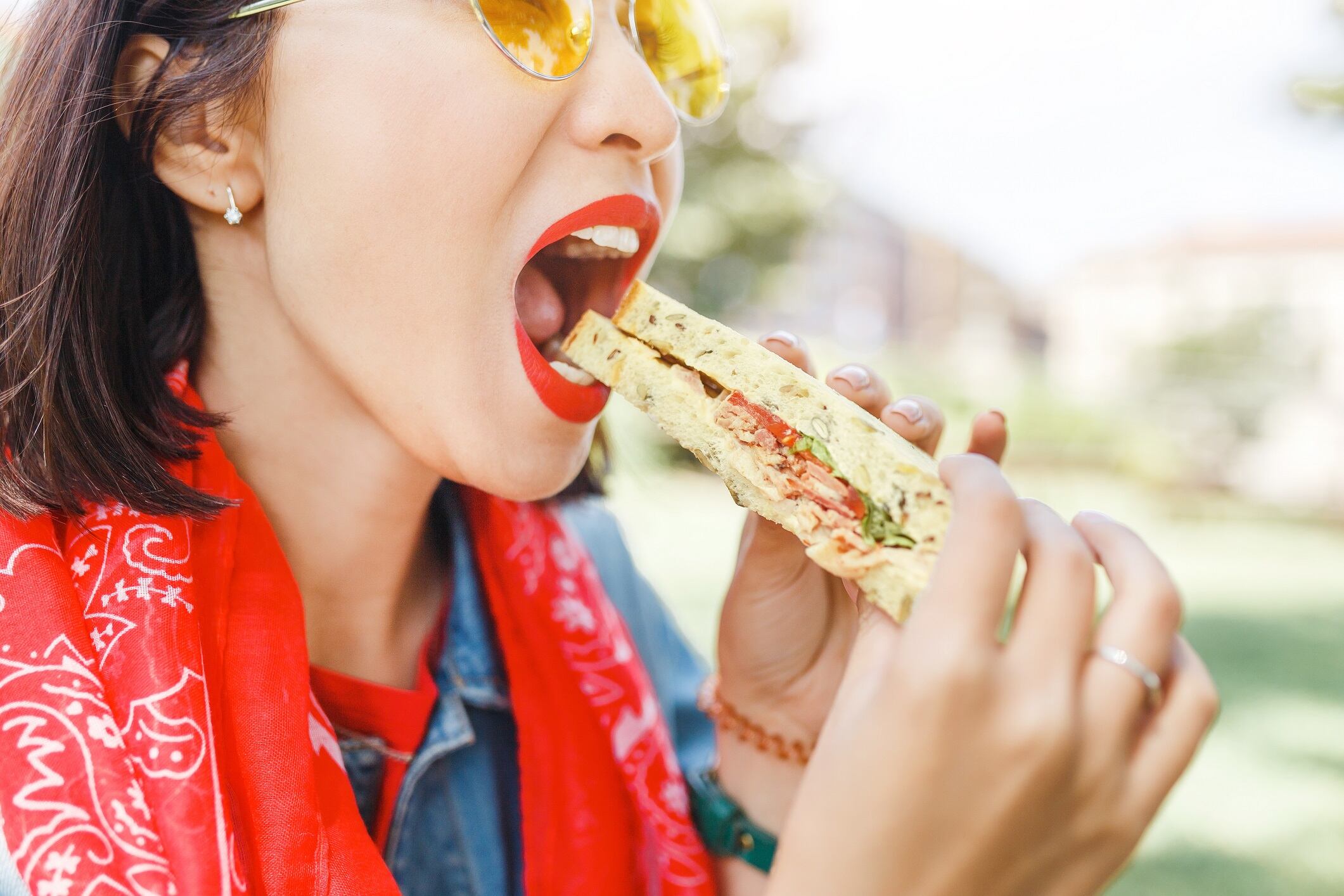 Young woman eating sandwich and having lunch break outdoors in park.