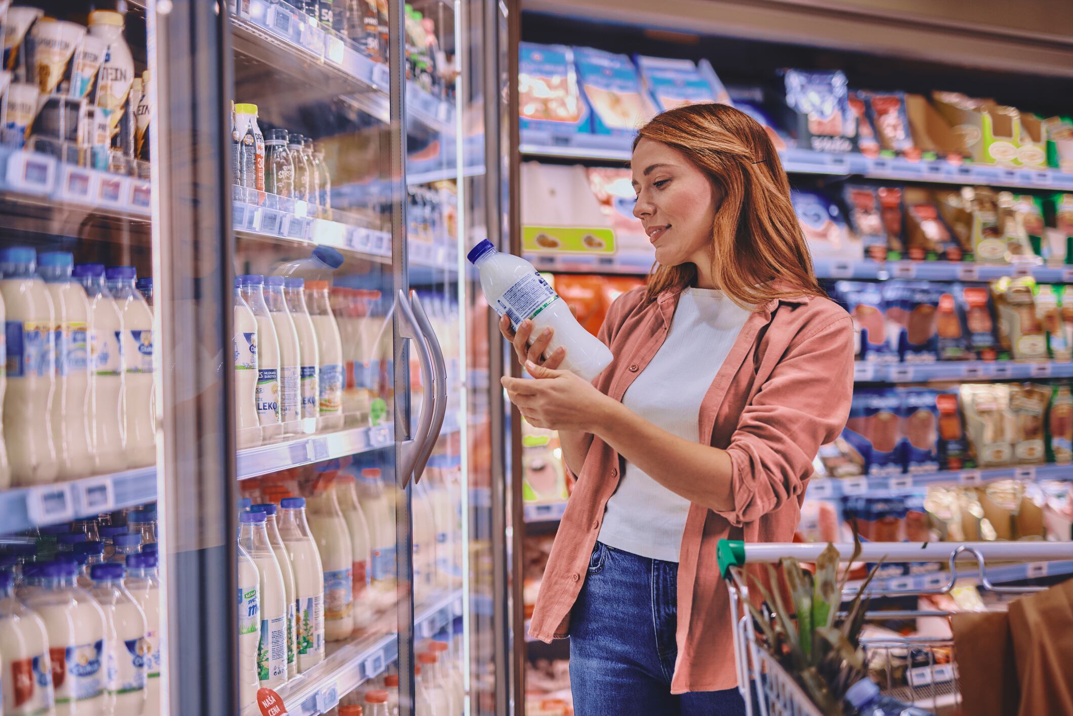 A smiling woman is reading the label on a bottle of fresh milk checking the sell-by date as she does her weekly shop in her local supermarket