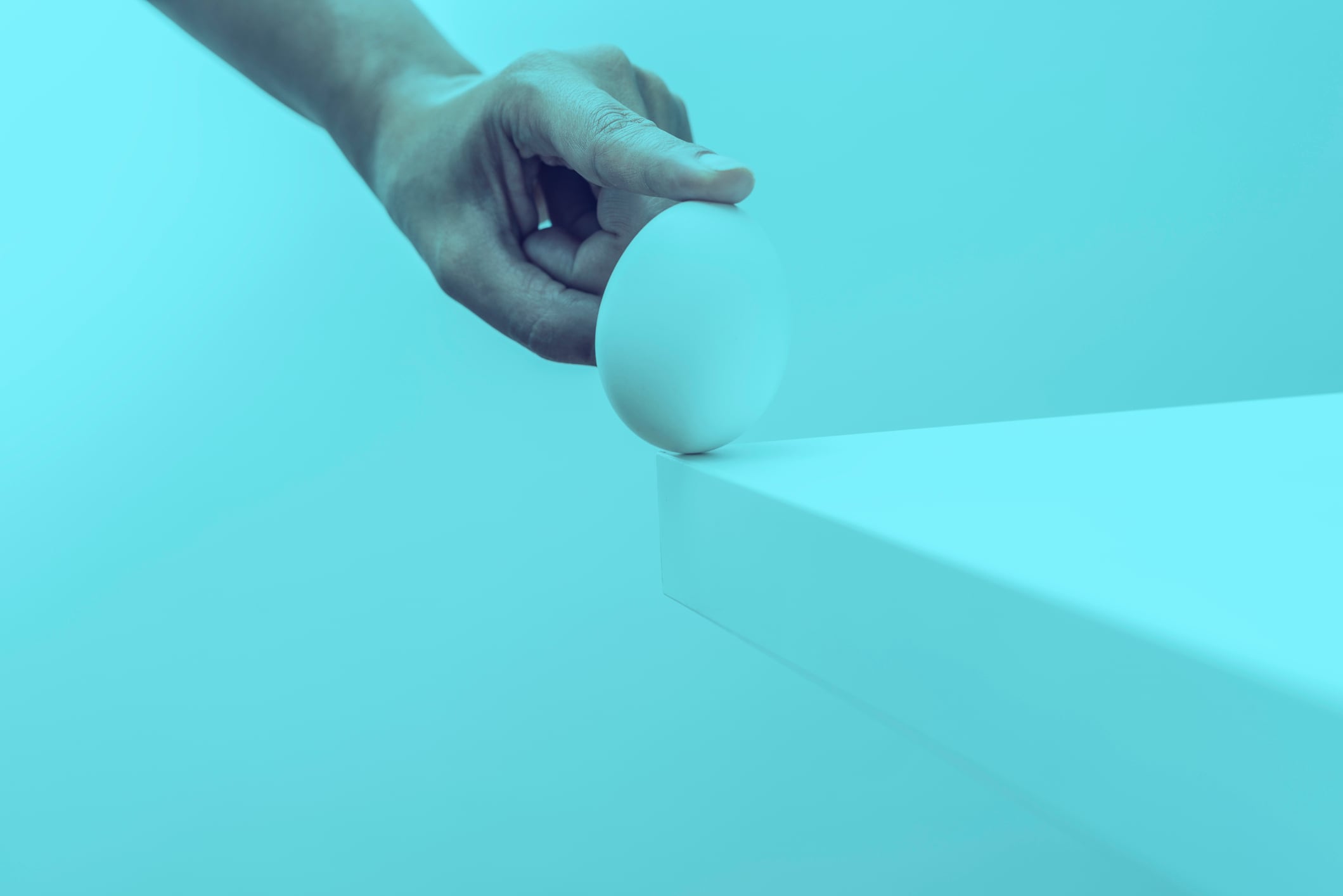 Finger touches an egg to protect from falling from table representing risk prevention.