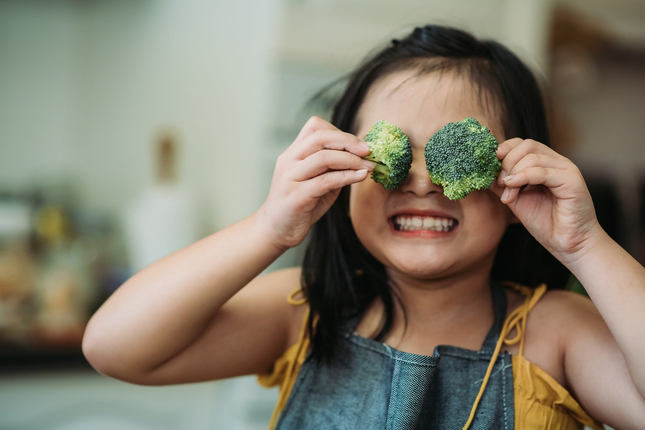 Little girl holding broccoli pieces over her eyes.
