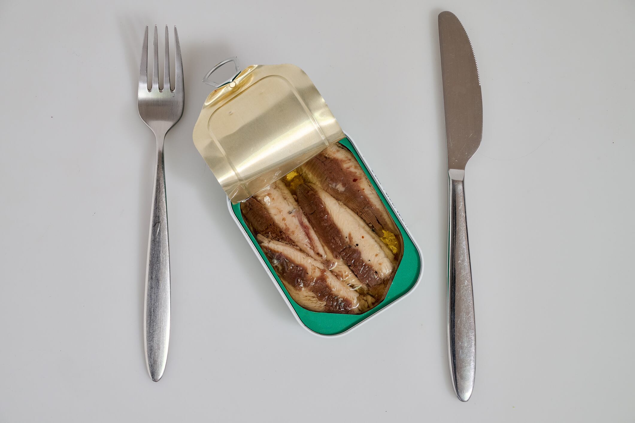 Metal Can of sardines in oil on white background with fork and knife