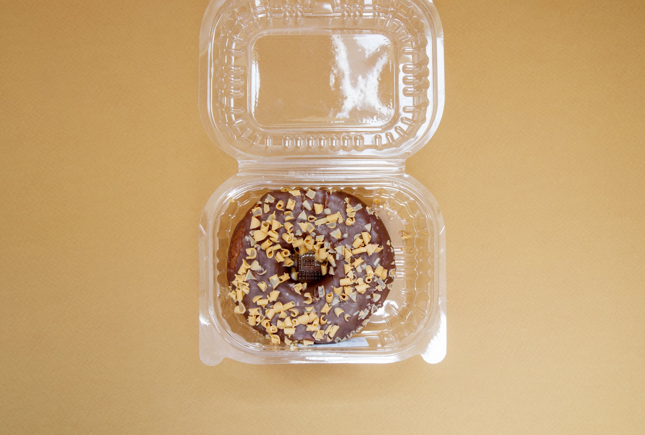 Chocolate donut in a plastic container on a brown or coffee background. Takeaway breakfast concept. One donut is packed in a plastic box for delivery. Sweet pastries delivered to your home. Top view